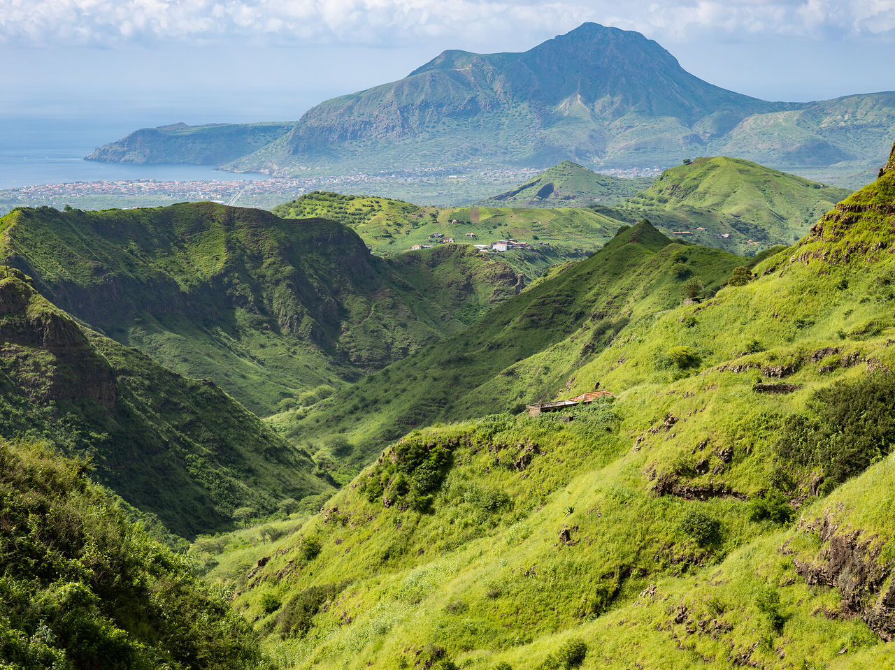 Paisaje con montañas verdes que se extienden hasta el horizonte, con la ciudad y el mar azul a lo lejos