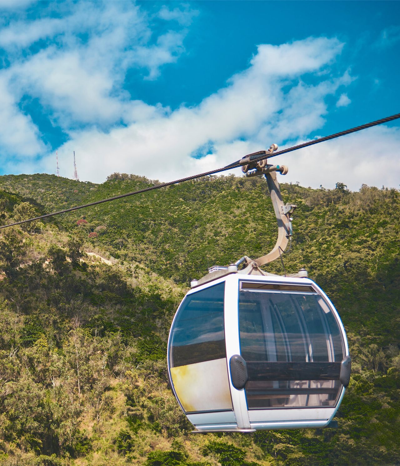 Cabina de teleférico moviéndose sobre una montaña en Caracas, rodeada de vegetación y con un cielo azul al fondo