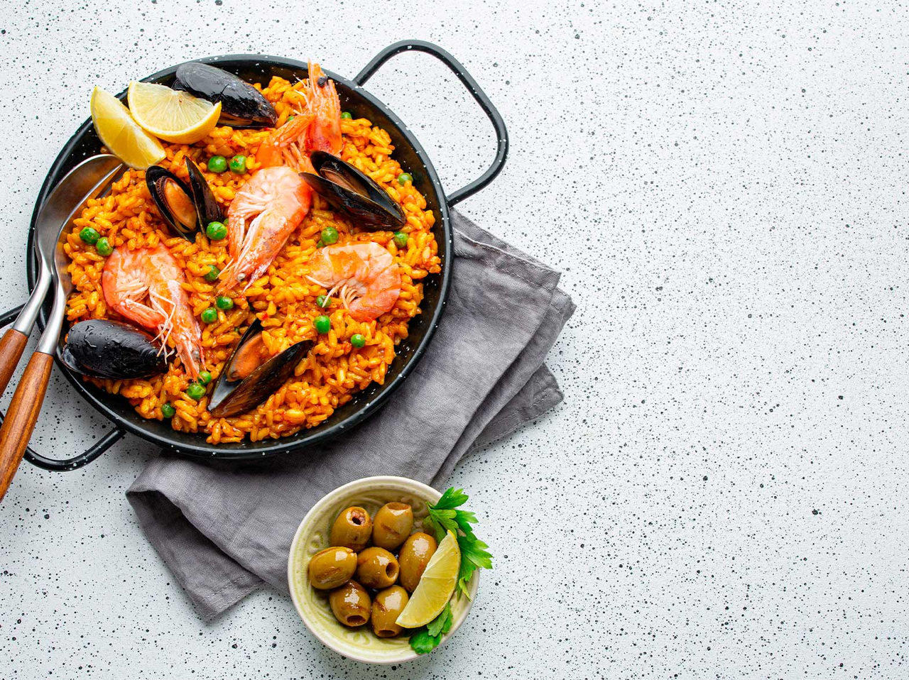 Plato típico de España, una paellera de paella, preparada con mejillones, camarones, guisantes y arroz, servida con aceitunas