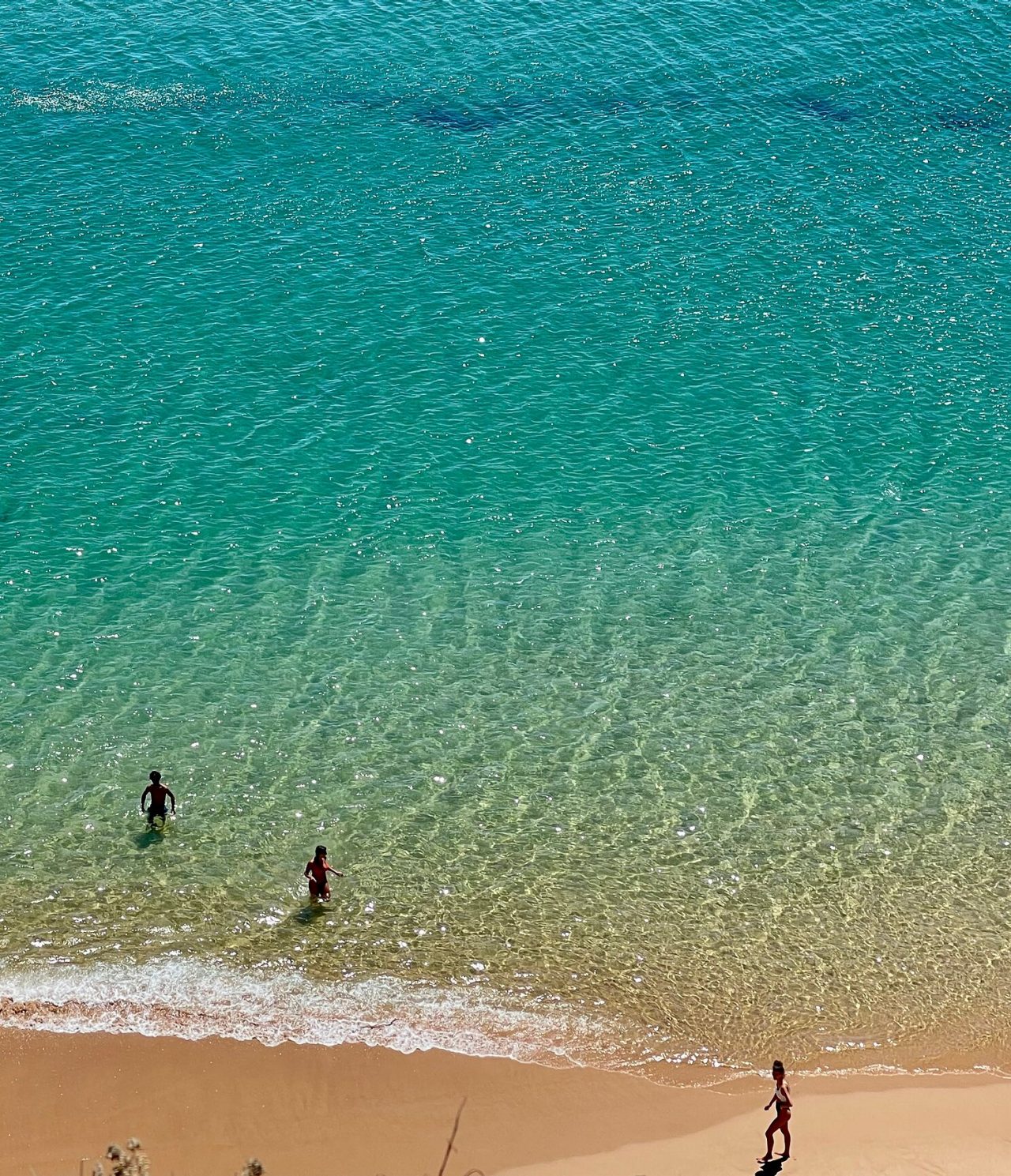 Vista aérea de dos personas nadando en una playa con aguas cristalinas y arena dorada, en la región del Algarve