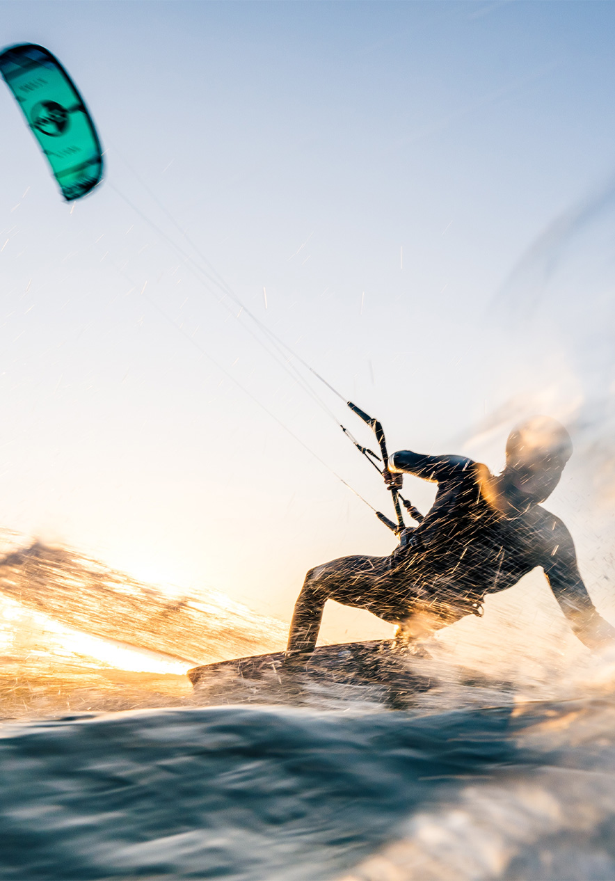 Hombre hace kitesurf en el mar con vela azul, agua salpicando y sol brillando