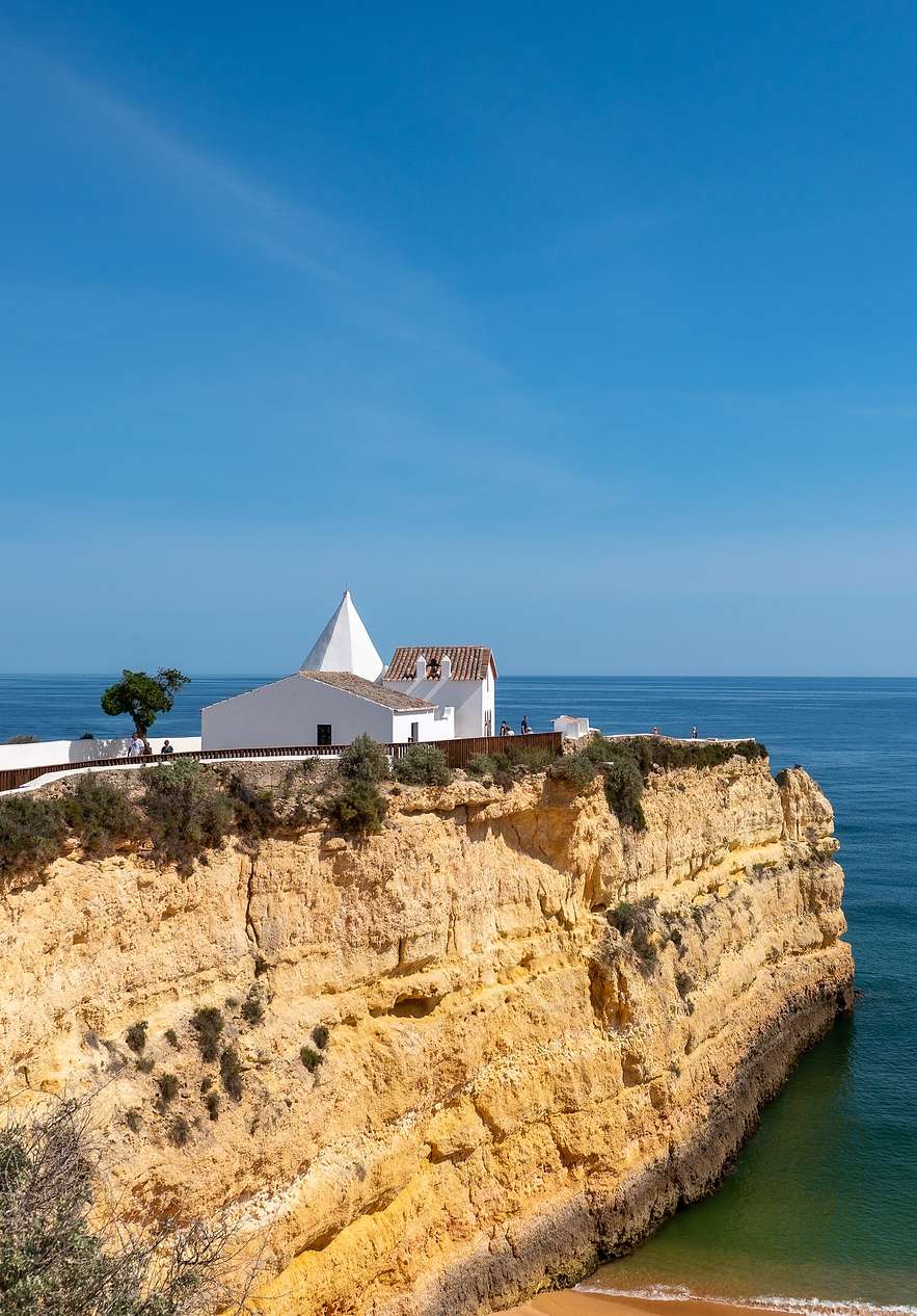 Vista de la falésia de la playa Senhora da Rocha, con una pequeña casa blanca y un mar calmado
