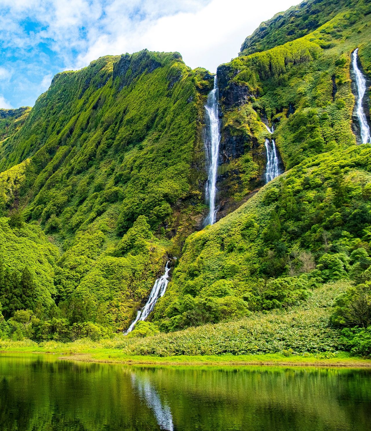 Cascada deslumbrante rodeada de montañas cubiertas de vegetación verde en la isla de Flores, Azores
