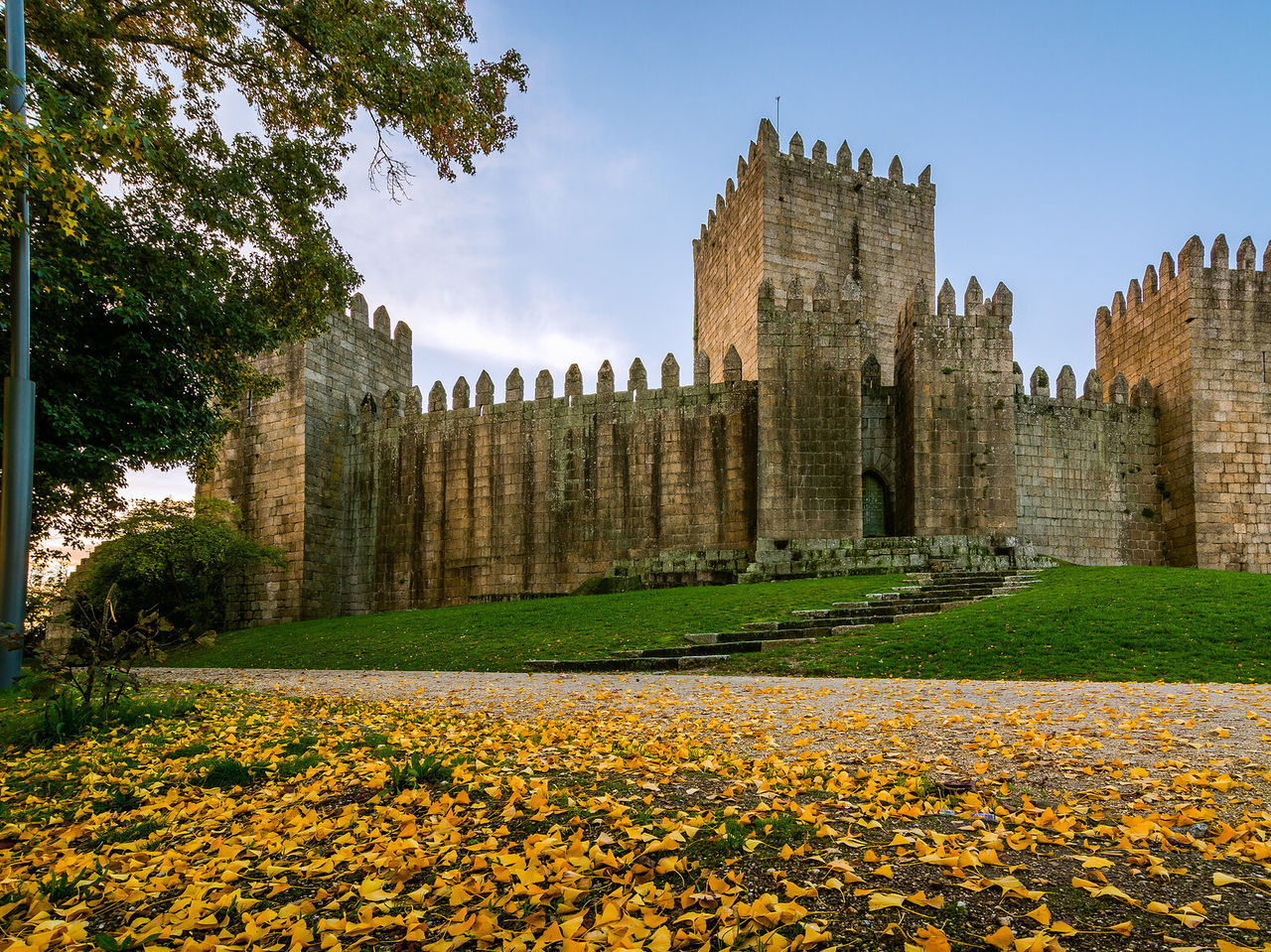 Castillo de Guimarães caracterizado por su arquitectura medieval, rodeado de hierba y hojas amarillas caídas