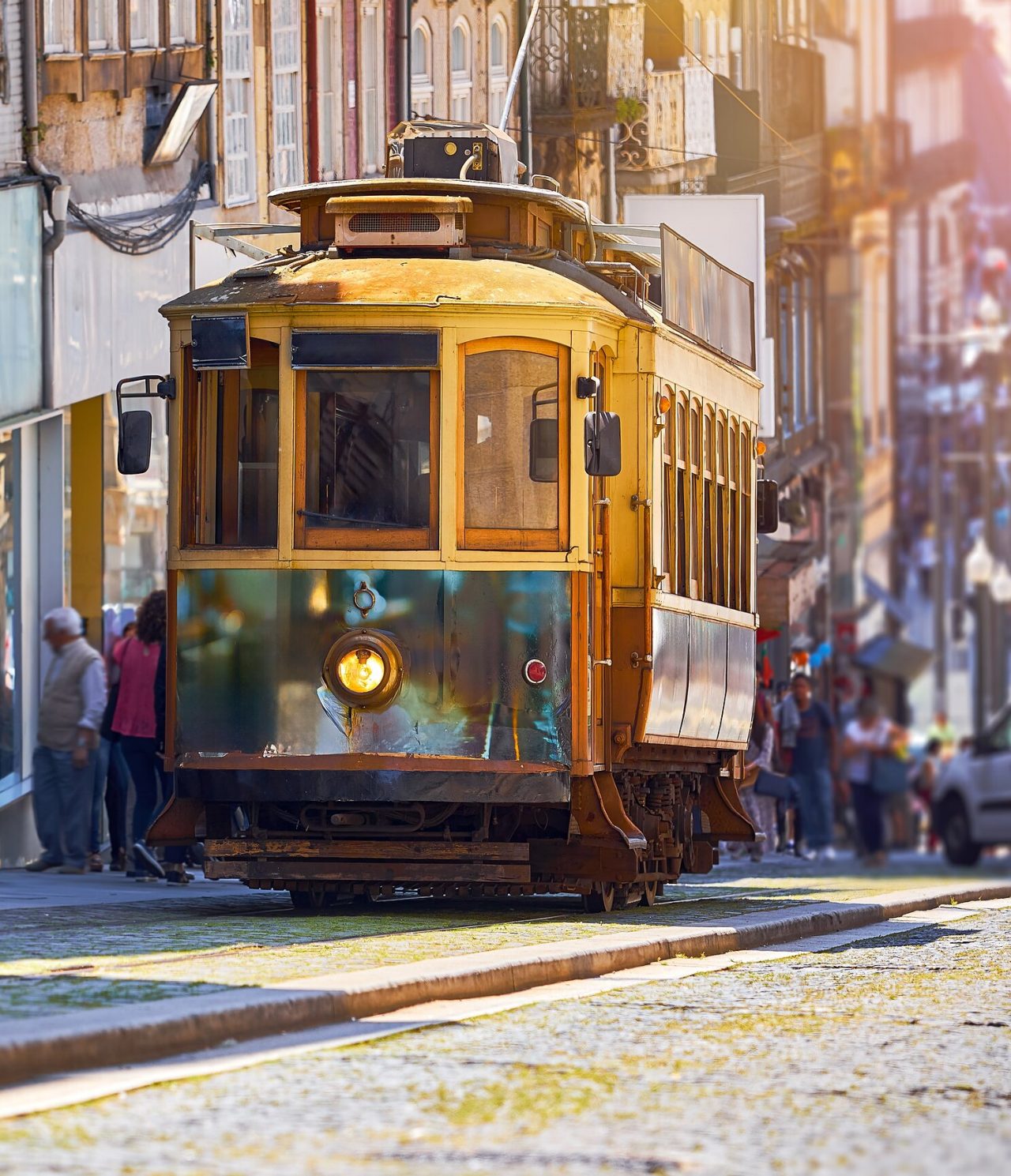 Vista de un antiguo tranvía amarillo subiendo una calle en Oporto, con varias personas detrás y edificios antiguos