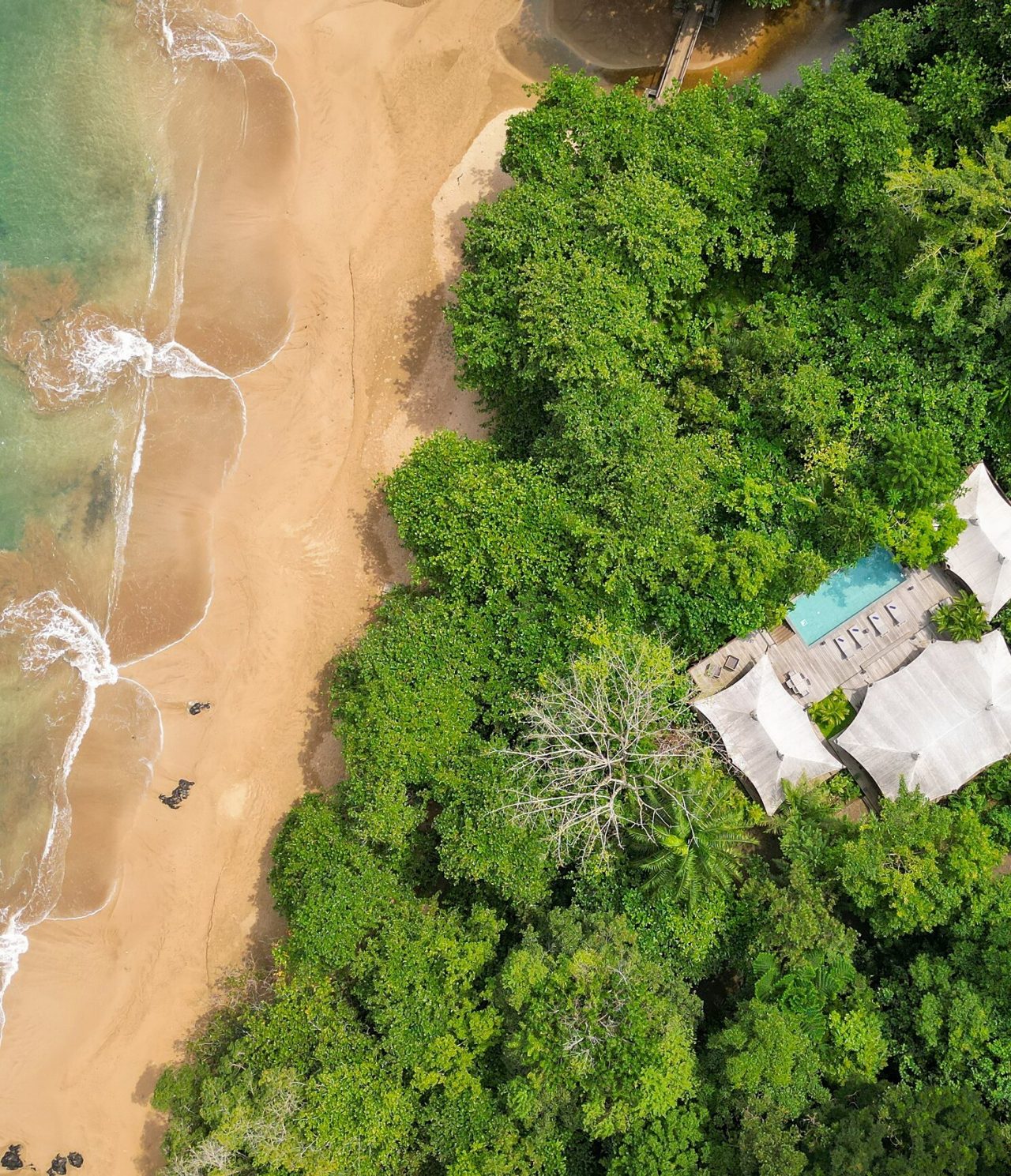 Vista aérea da ilha de São Tomé e Príncipe, com um edifício com piscina e uma praia de areia branca com águas cristalinas