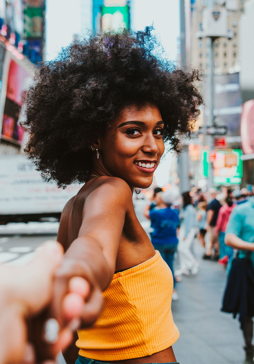 Mulher sorridente a segurar a mão de um pessoa, em Times Square, com letreiros luminosos e pessoas ao fundo.