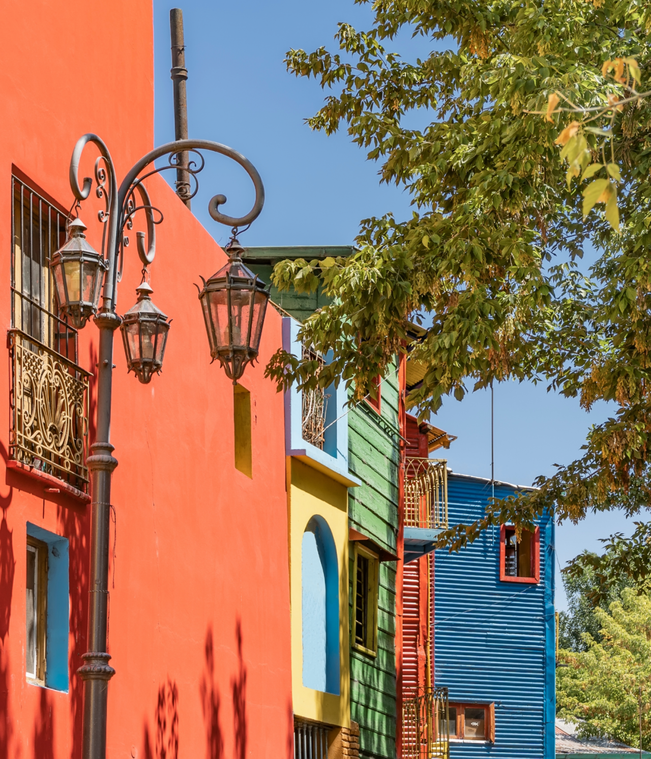 Edifícios coloridos do bairro típico do Caminito, em Buenos Aires, com árvores em frente e um céu azul por trás