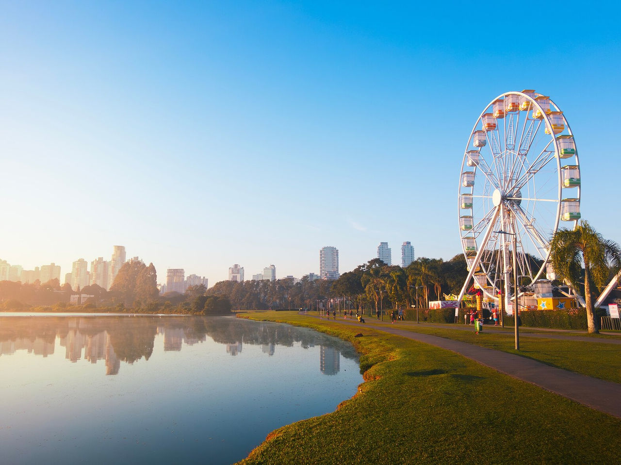 Vista urbana pitoresca com a roda-gigante de Curitiba refletida nas águas do lago e a cidade ao fundo num dia ensolarado
