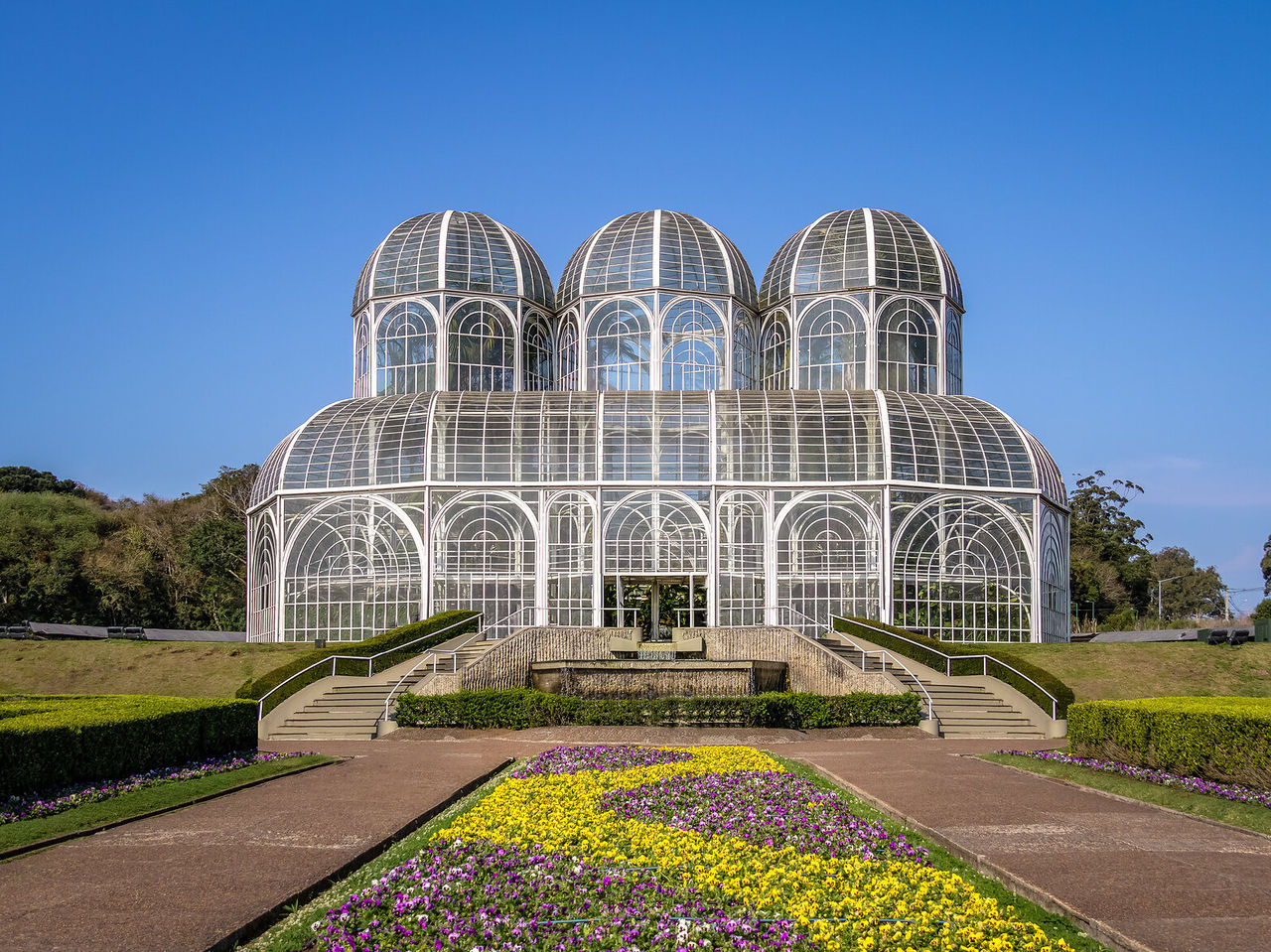 Vista frontal da imponente estufa do Jardim Botânico de Curitiba com os seus jardins floridos e coloridos
