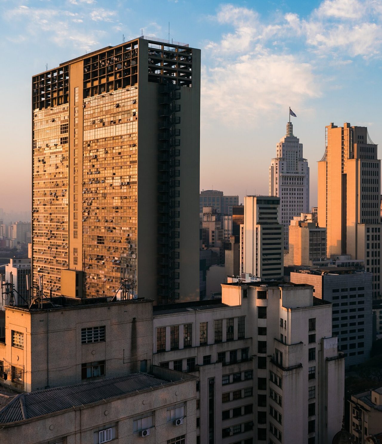 Vista de vários edifícios altos em São Paulo, no Brasil, com o sol a bater nas janelas e um céu azul por trás