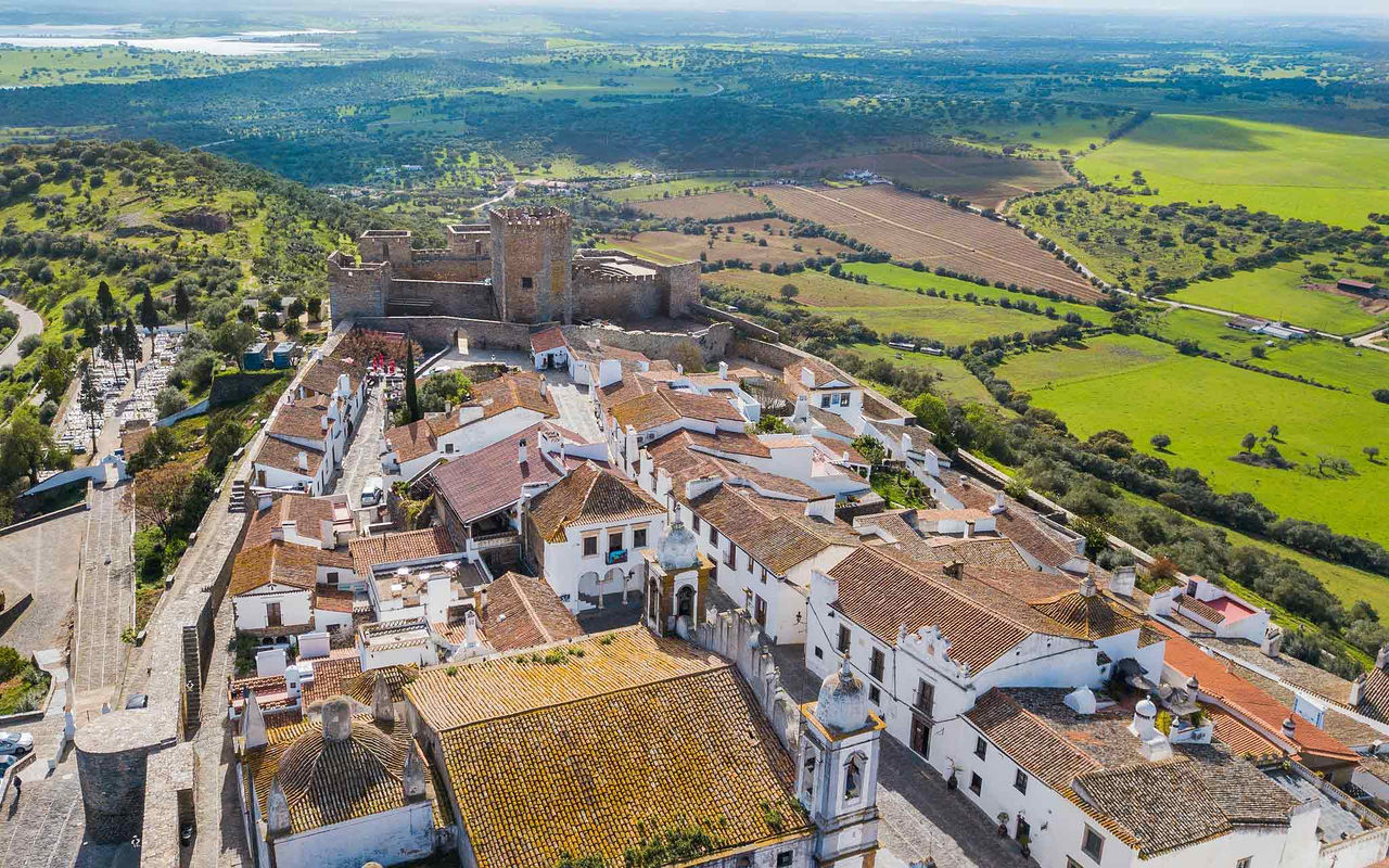 Vista aérea da vila histórica de Monsaraz, no Alentejo, com destaque para o castelo no topo da colinaVista aérea da vila histórica de Monsaraz, no Alentejo, com destaque para o castelo no topo da colina