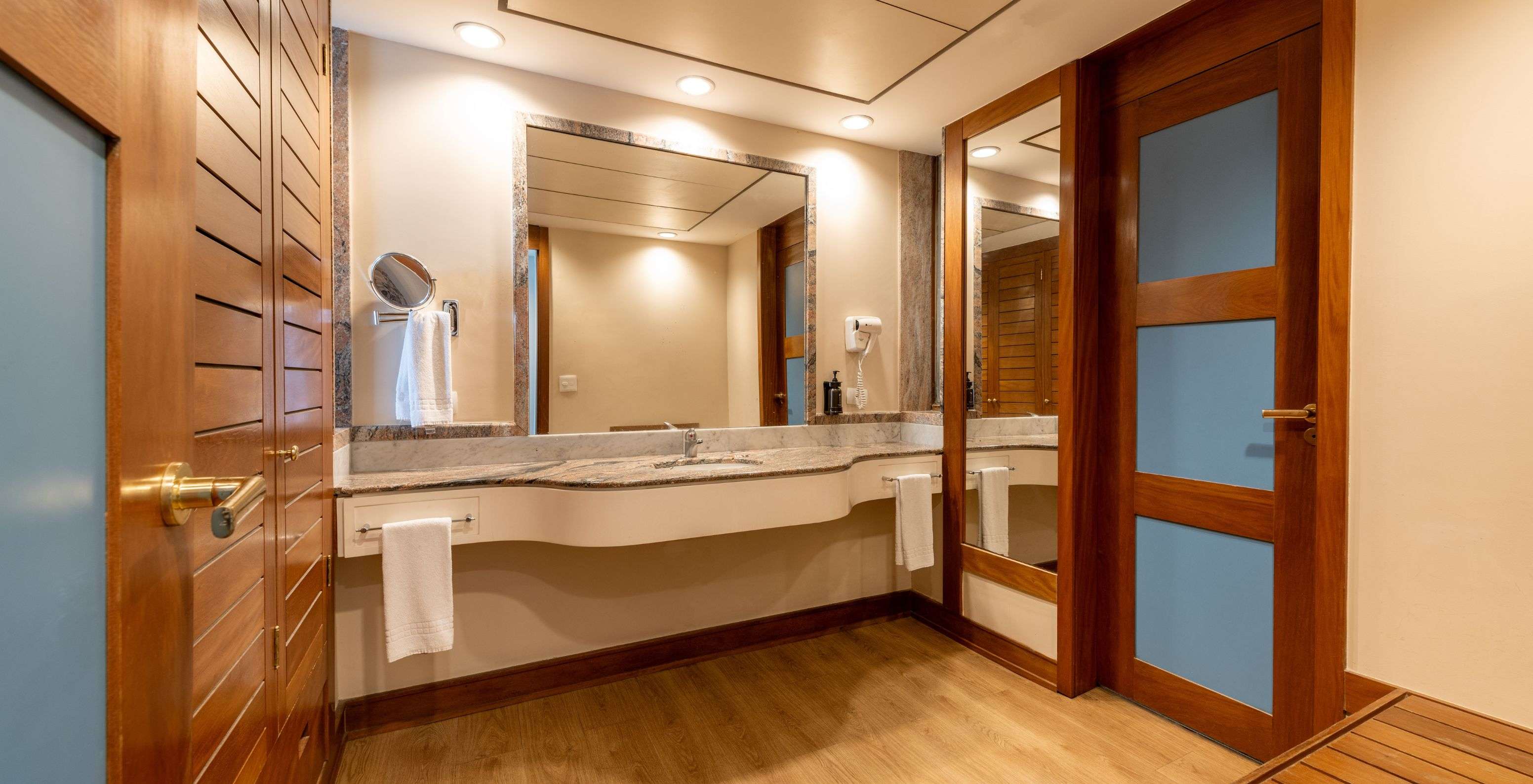 The Deluxe at Pestana São Paulo has a bathroom with a large sink with a mirror, a hairdryer, and towels