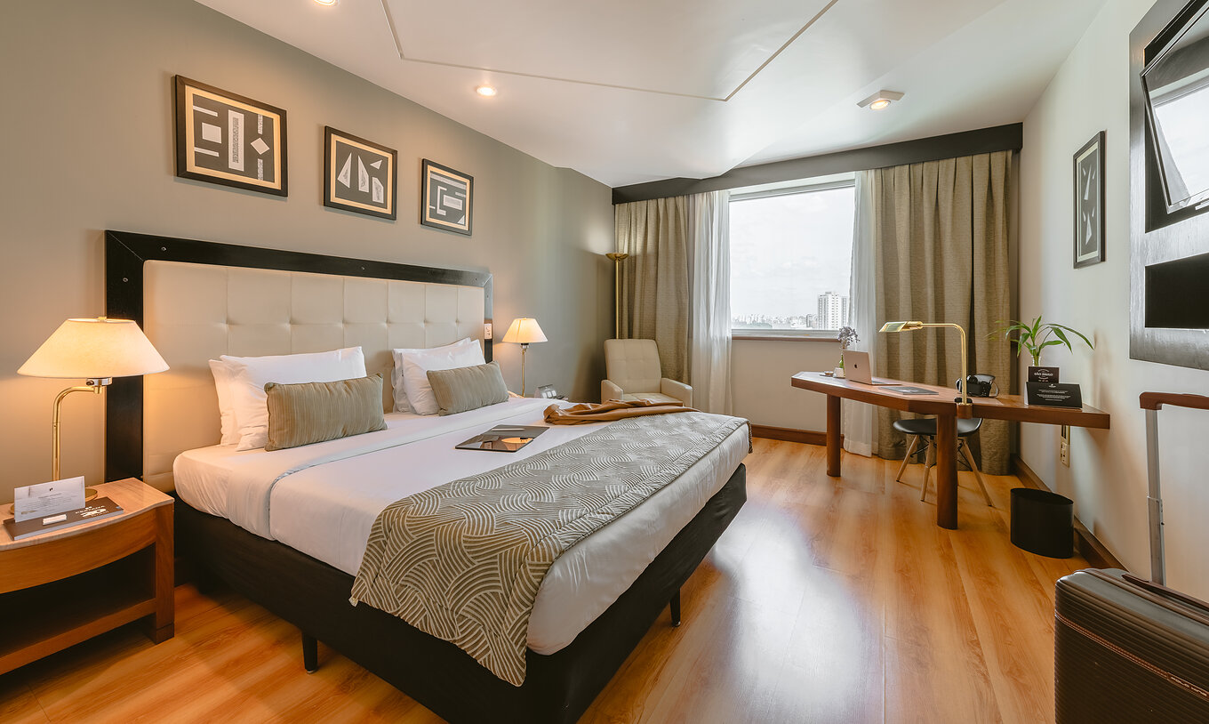 The Queen Standard of Pestana São Paulo has a double bed, two bedside tables, an armchair, and a desk