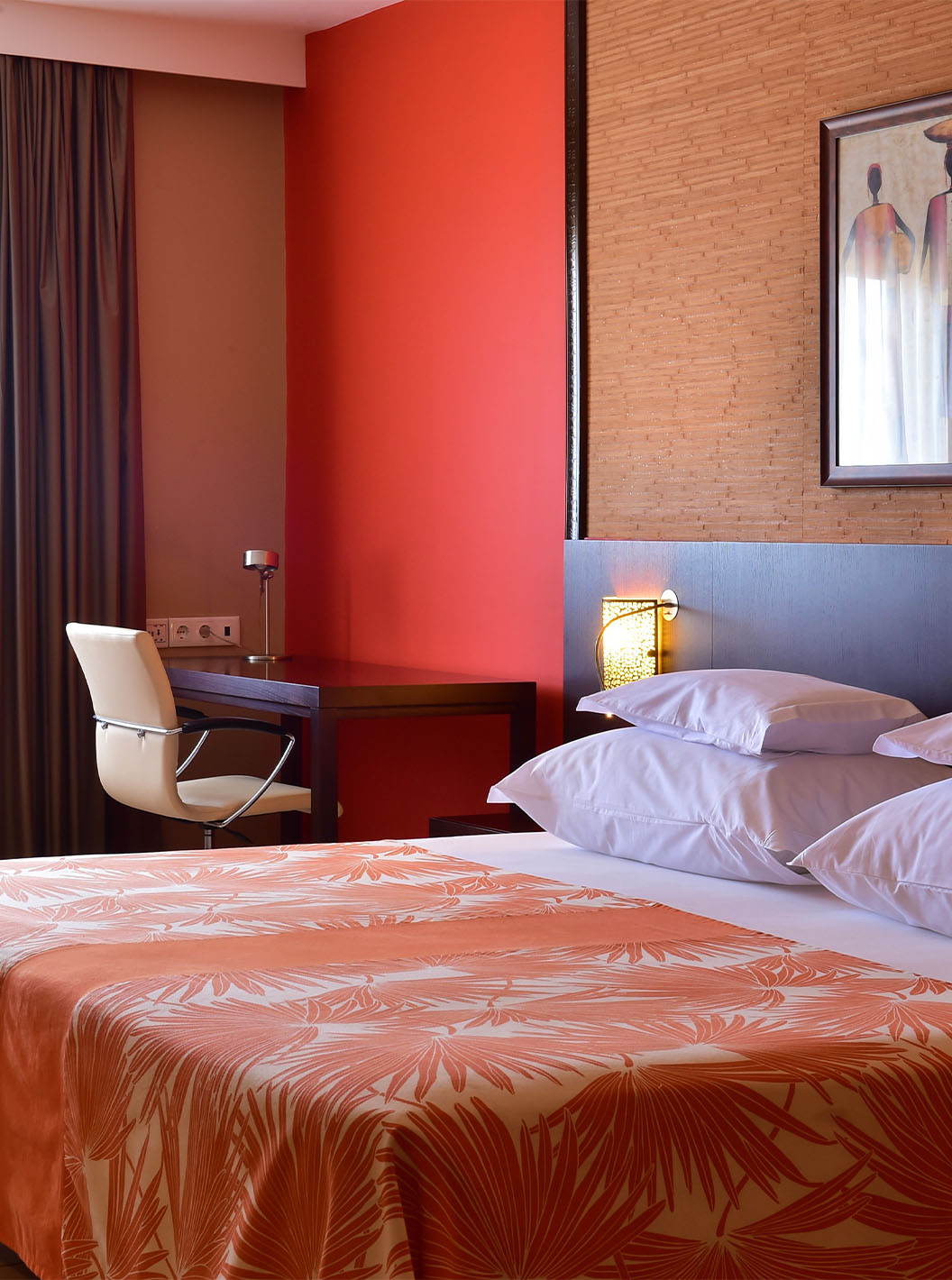 The Standard room at Pestana Tropico features a double bed, desk with chair, and bedside table with lamp