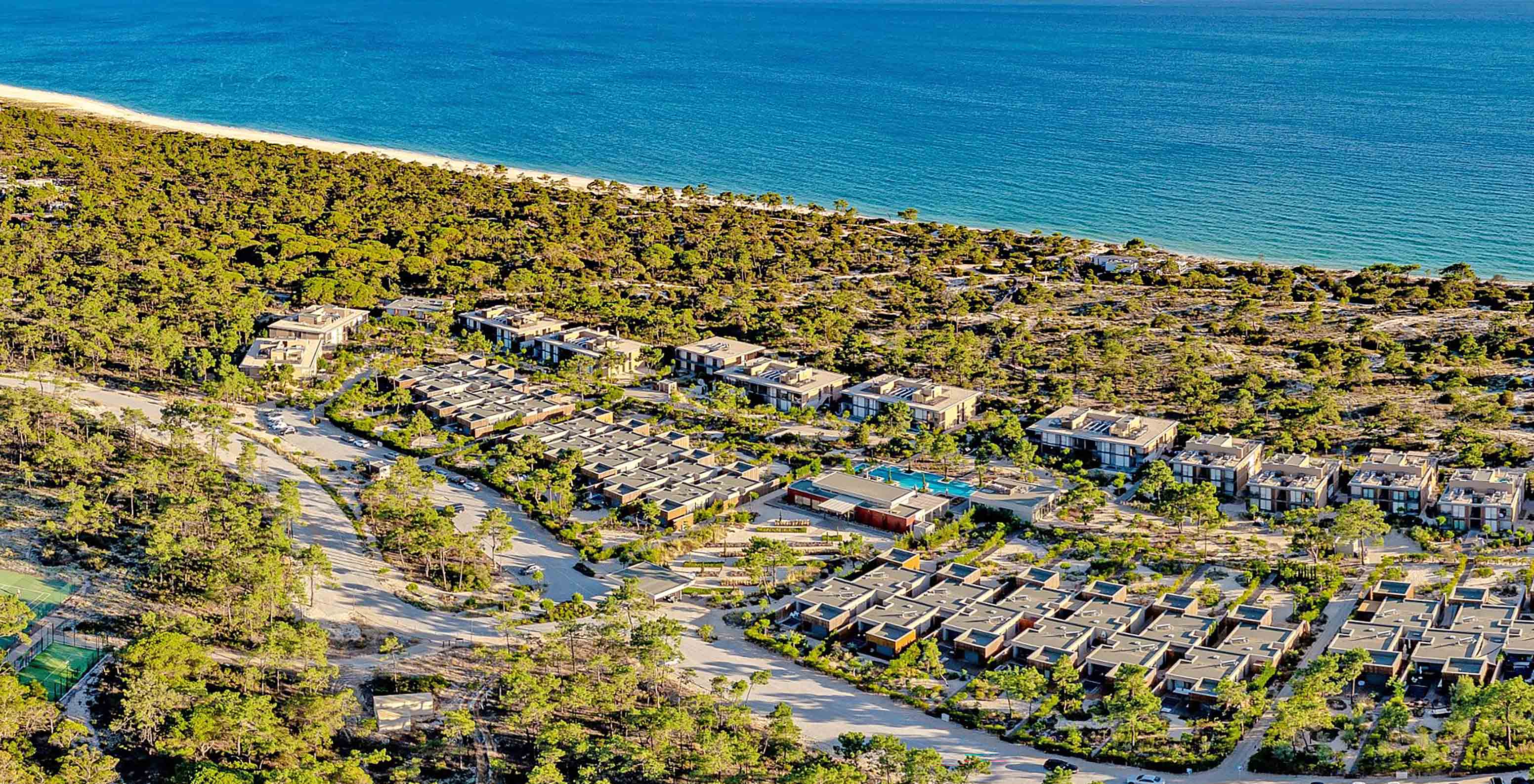 Aerial view of Pestana Tróia Eco Resort near the beach, surrounded by greenery and several houses