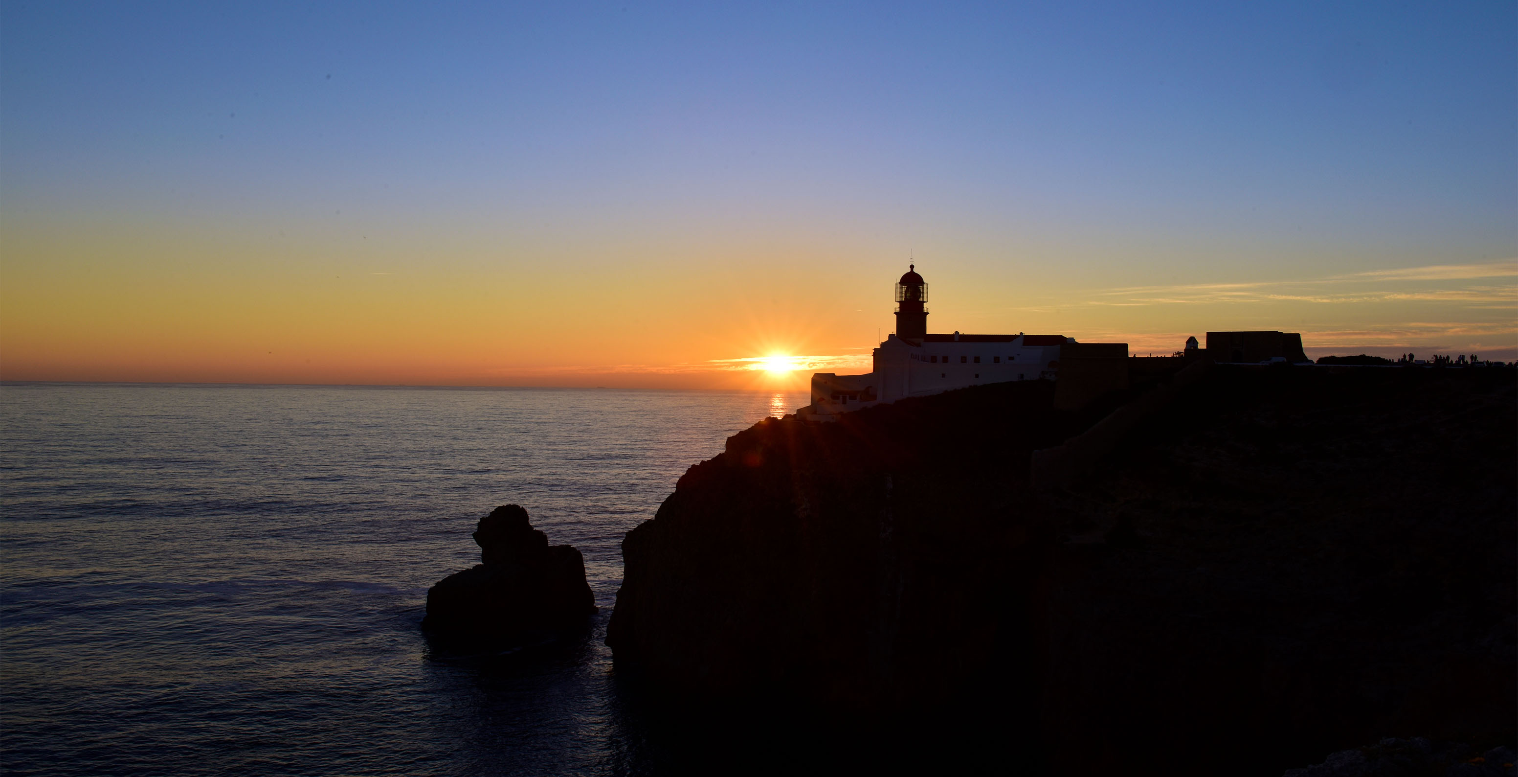 Sunset cliff view with orange horizon, lighthouse on cliff top