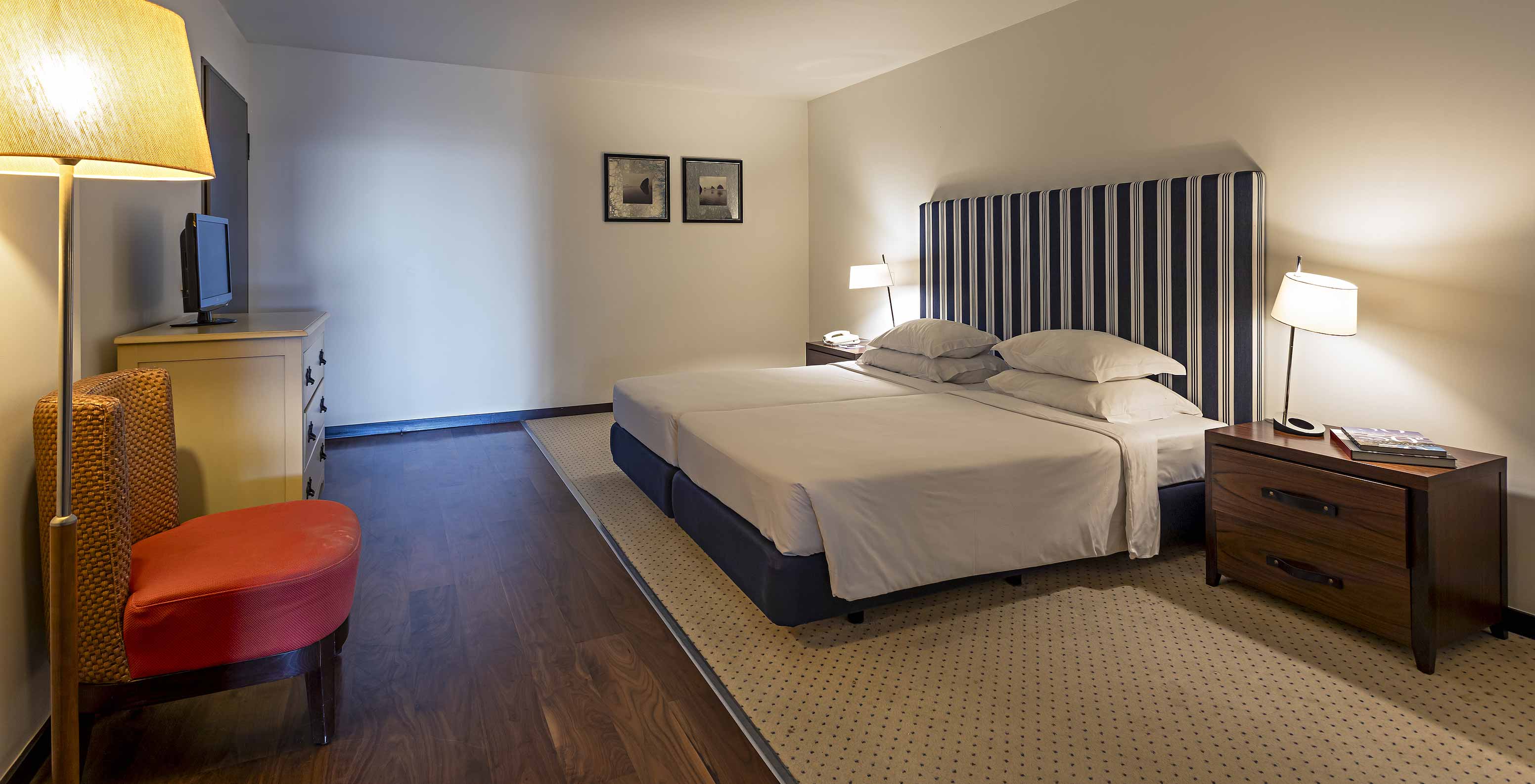 The Cliff Suite T2 at Pestana Alvor Praia has a large bedroom with a double bed, two paintings, and a dresser with a TV