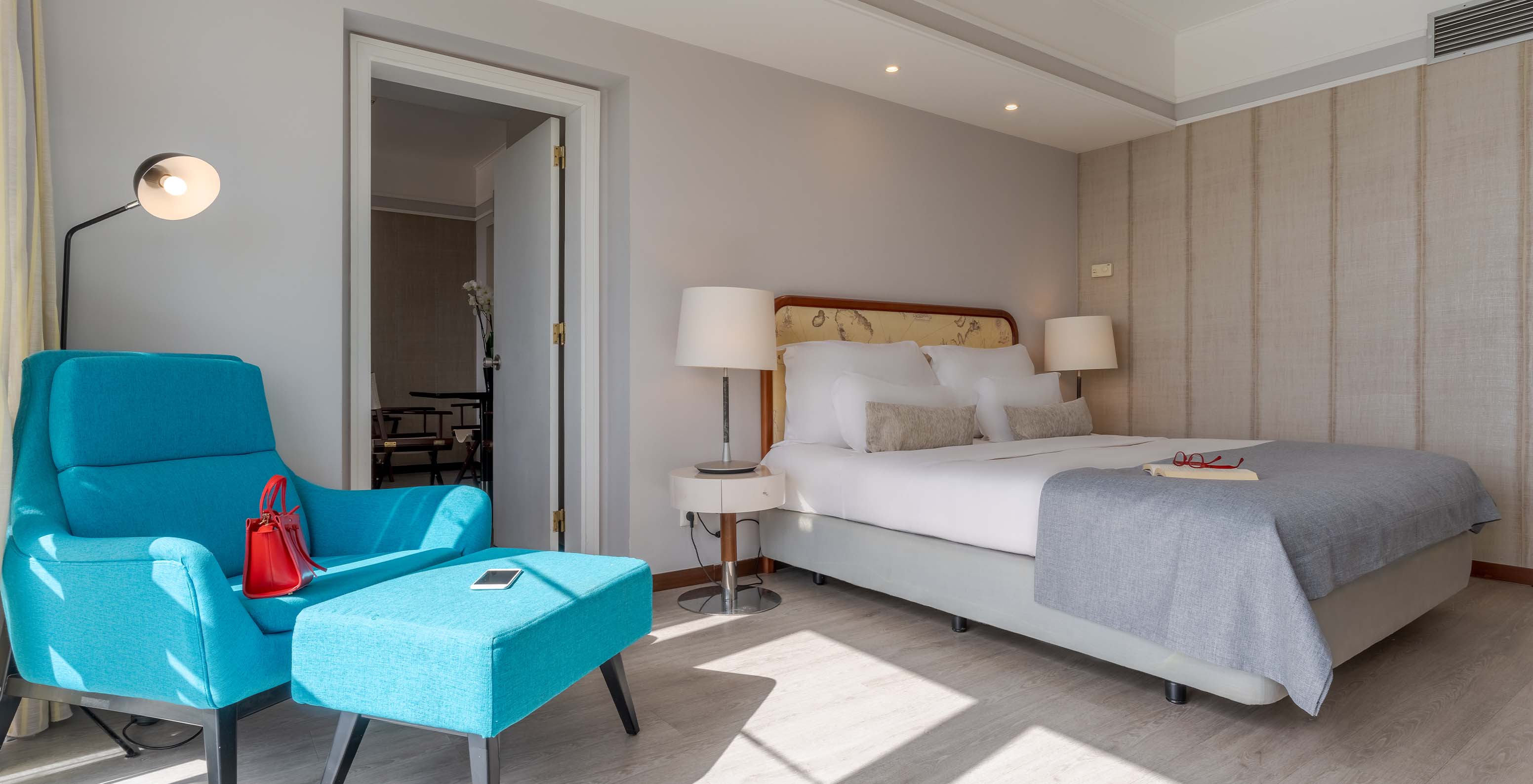 The Sea View Suite at Pestana Alvor Praia has a double bed with a blue armchair, lamps, and wooden flooring