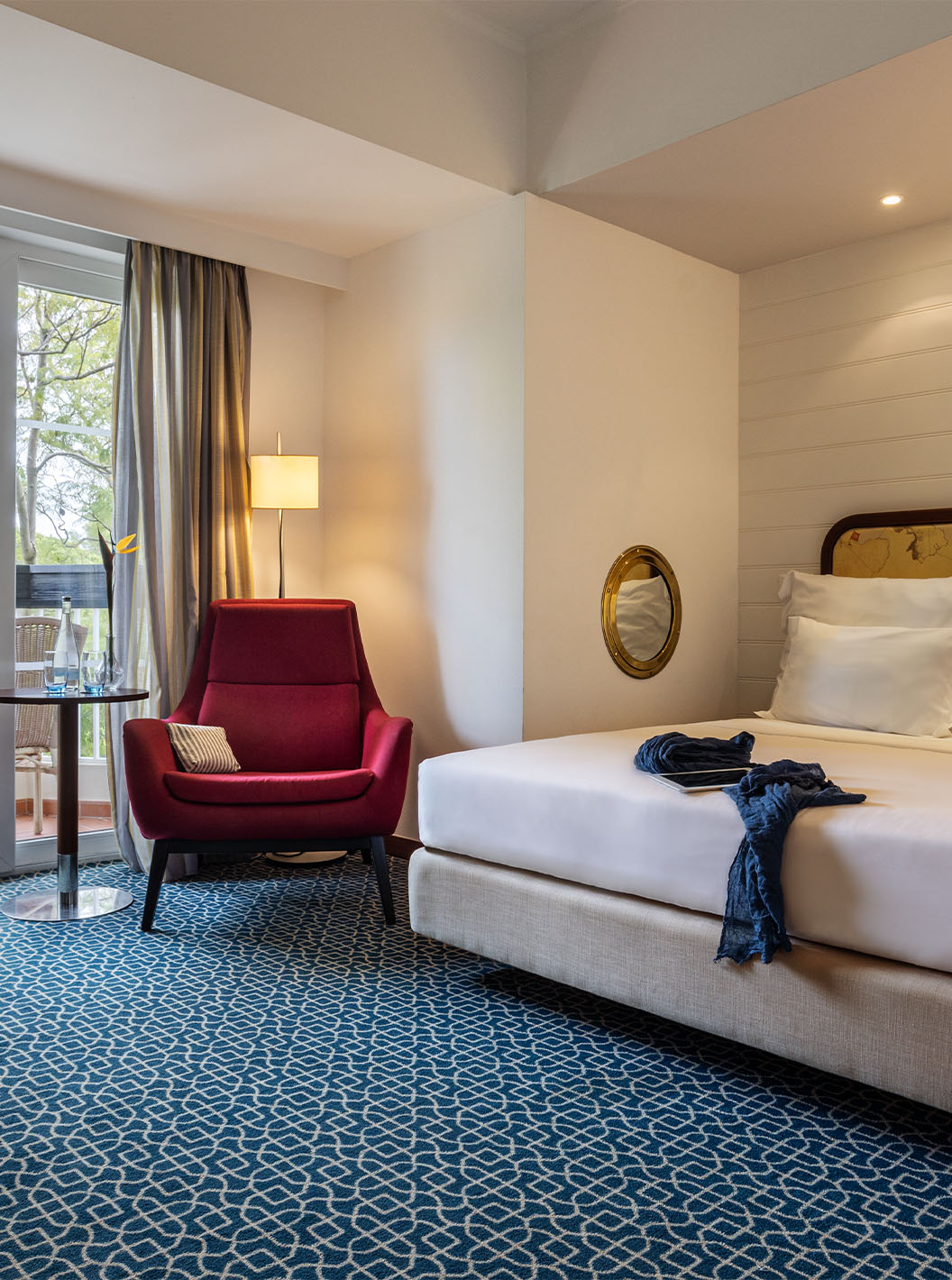 The Garden View Suite at Pestana Alvor Praia has a double bed, a red armchair, and a view with chairs