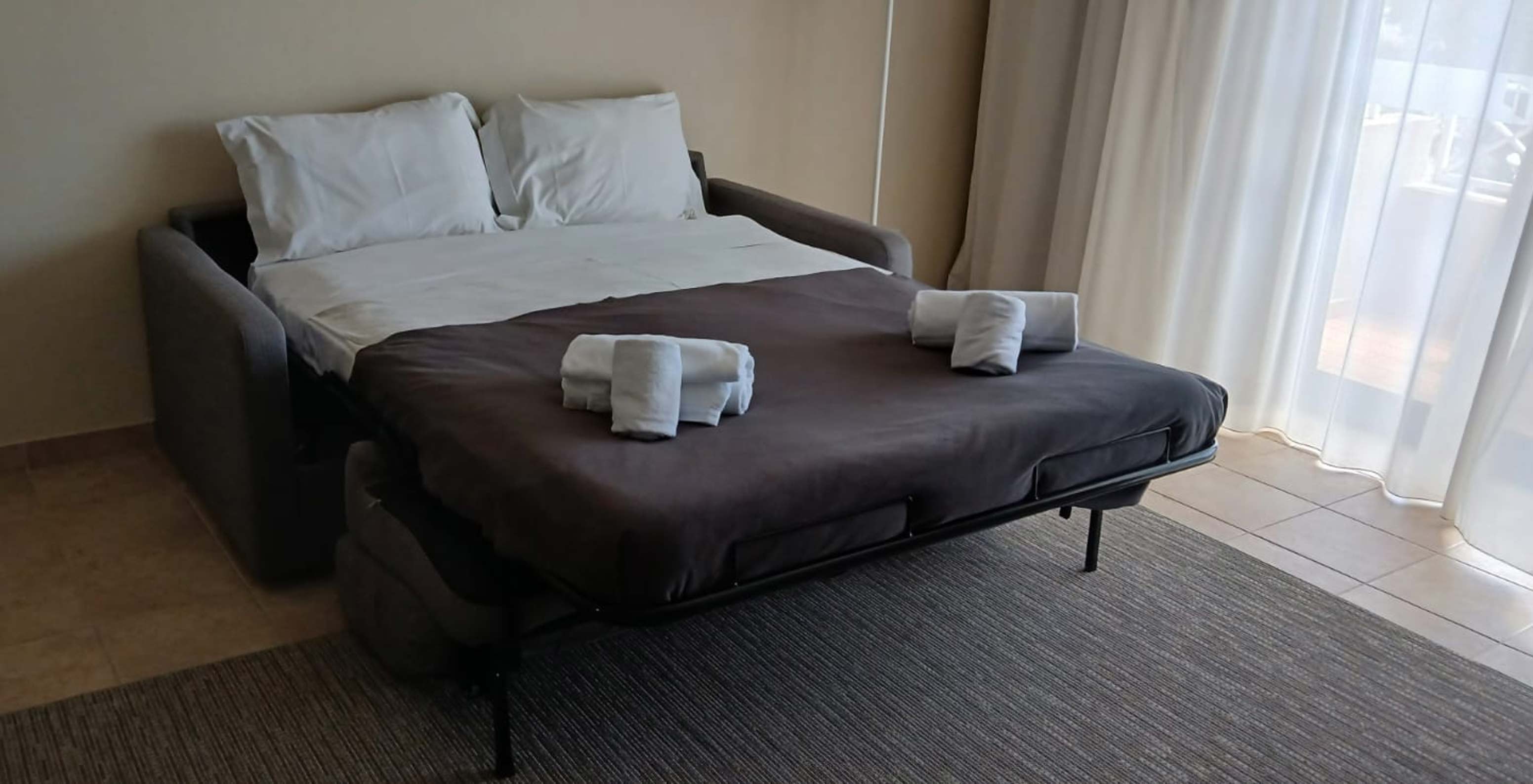The studio at Pestana Gramacho Residences has an open sofa bed with white sheets and folded towels