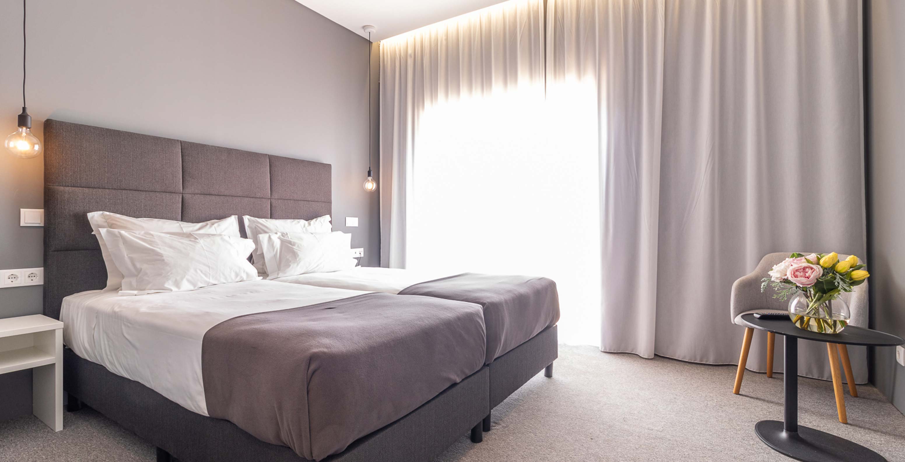 Classic Room at Pestana Gramacho Residences with two beds, grey curtains and table with flowers