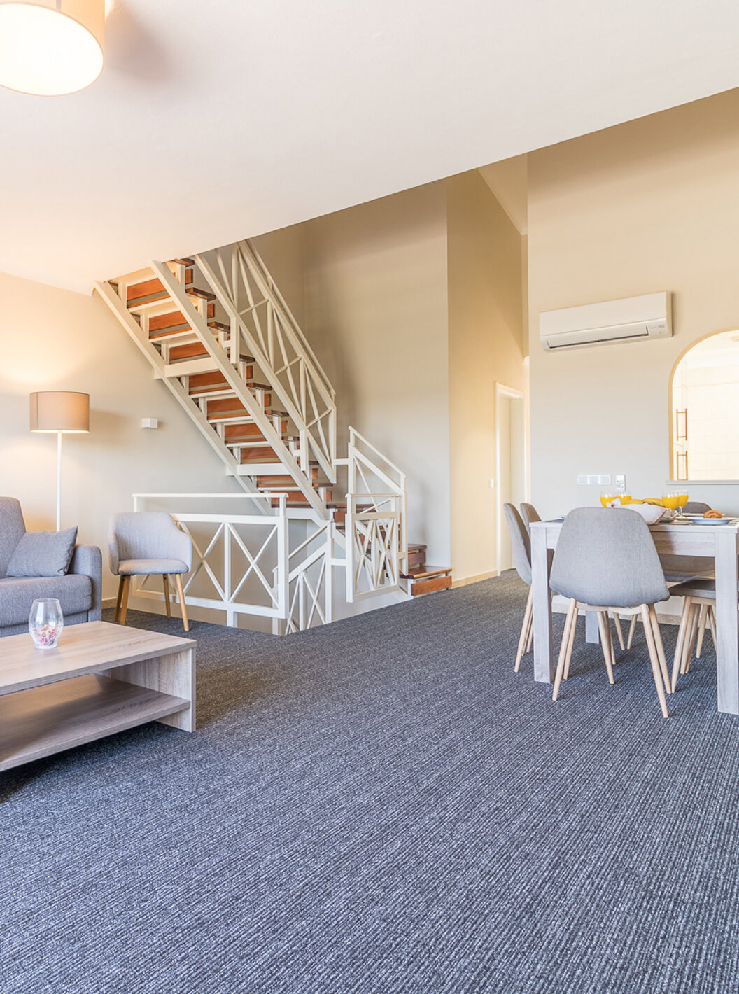 The two-bedroom apartment at Pestana Gramacho has a living room with grey sofa, coffee table and stairs in the back