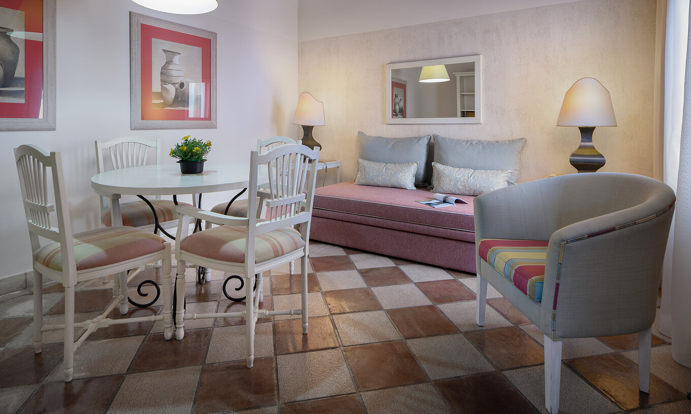 The Suite Garden View at Pestana Vila Sol - Vilamoura has a living room with sofa, table, chairs and a mirror