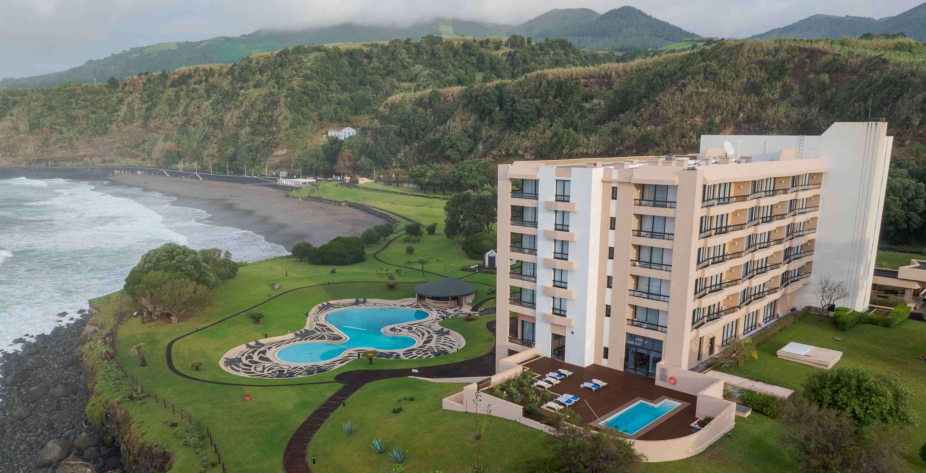 Aerial view of Pestana Bahia Praia with hotel, organic pool, gardens, and rocky coast in the background