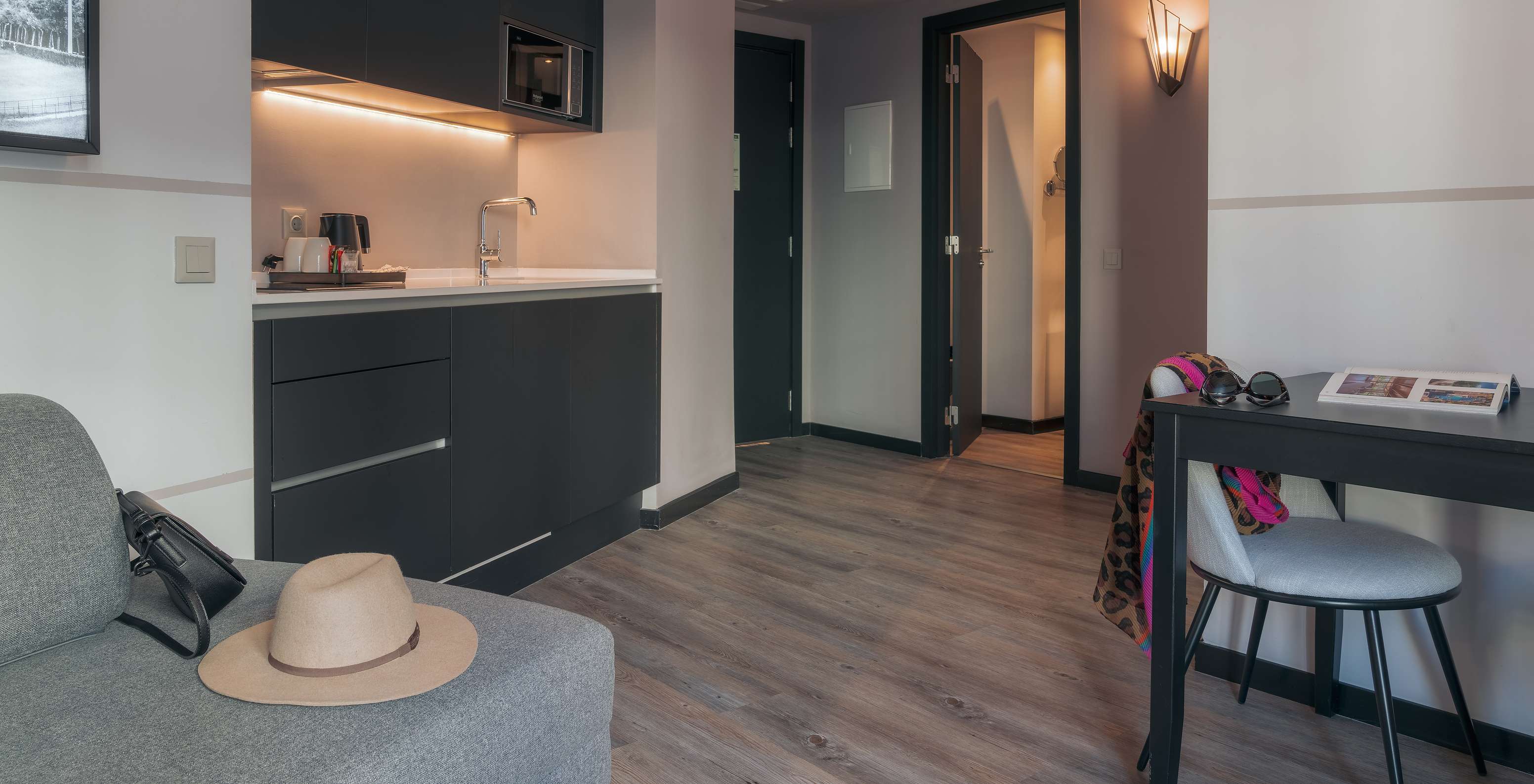The Double Deluxe Studio at Pestana Lisboa Vintage has a kitchenette with microwave, a table with chair and a gray sofa