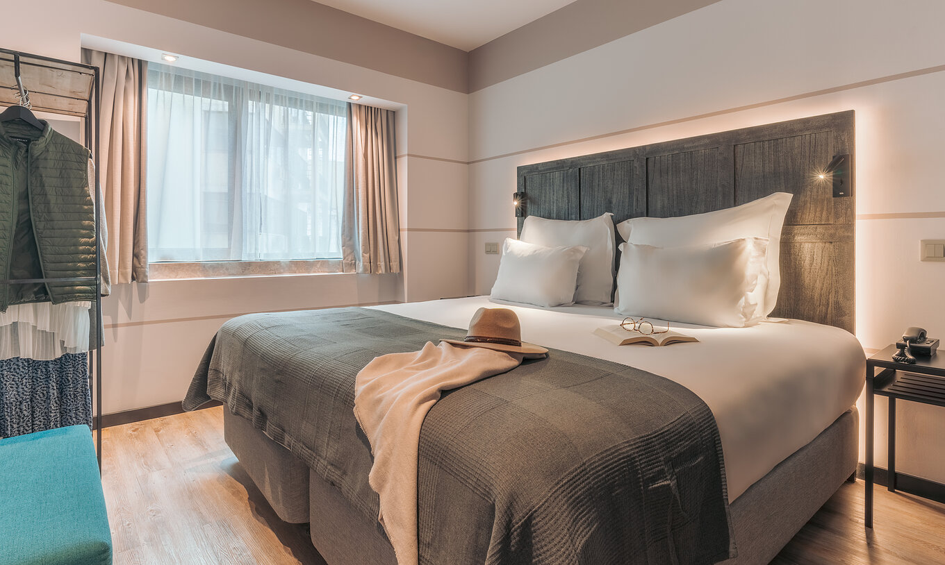 The Junior Suite at Pestana Lisboa Vintage has a double bed with a blanket, a blue sofa, bedside table and a wardrobe