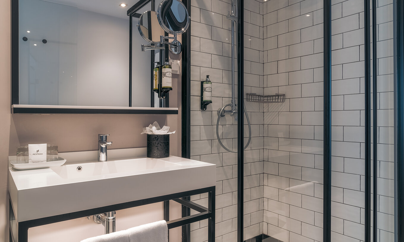 The Vintage Room at Pestana Lisboa Vintage has a shower with glass doors and black details and a sink with two mirrors