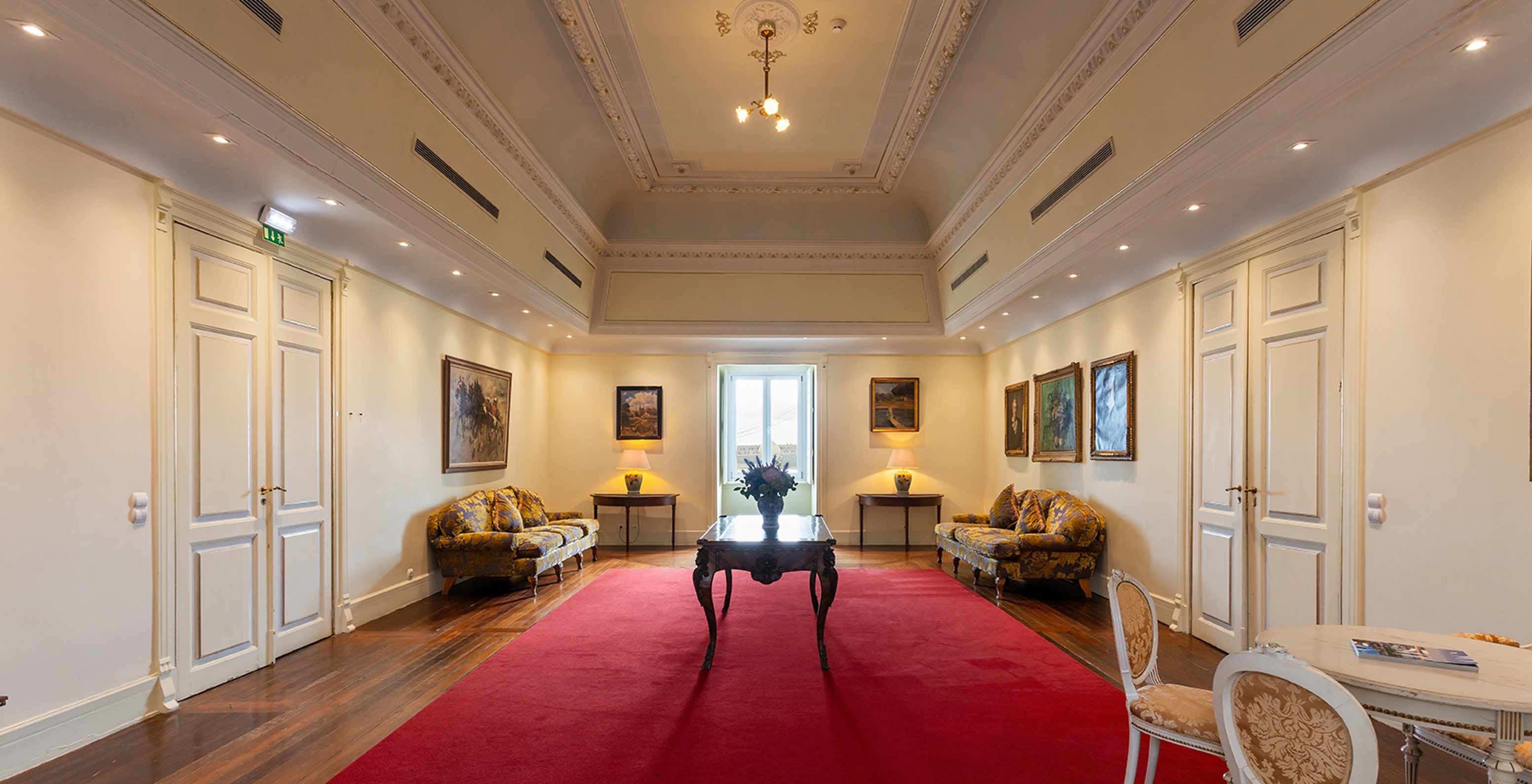 Pestana Palace Lisboa has a foyer with a large red carpet, two sofas and a window in the corner