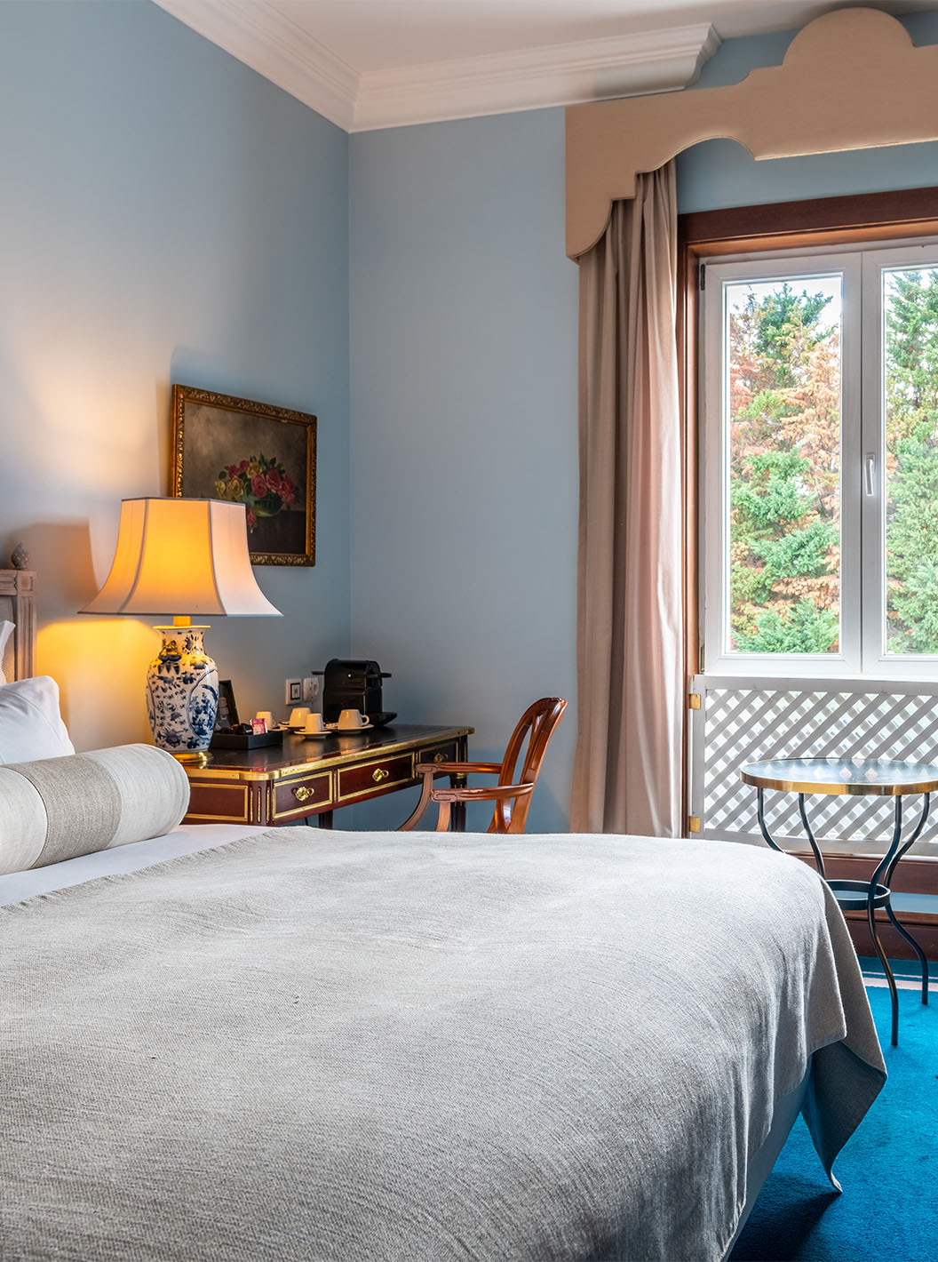 The Deluxe room at Pestana Palace Lisbon includes a double bed, a desk, a window with a decorative grille, and a blue carpet