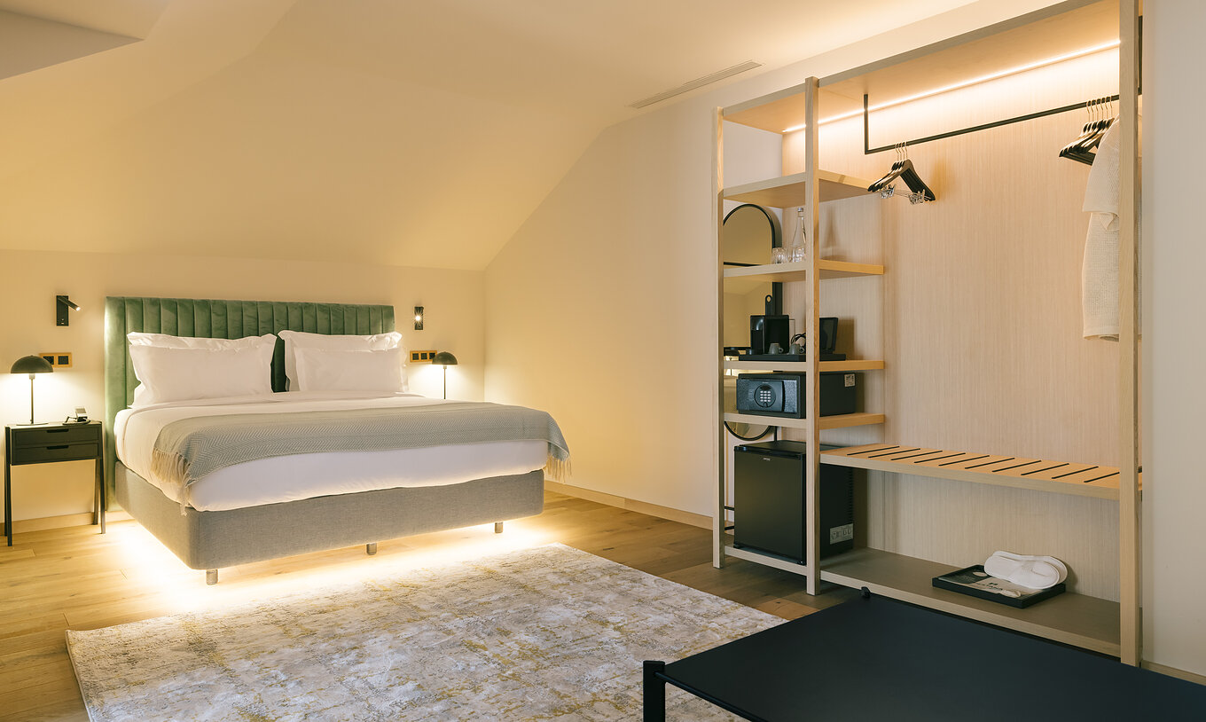 The Junior Suite of Pestana Rua Augusta Lisboa has an illuminated double bed and an open wardrobe with hangers and shelves