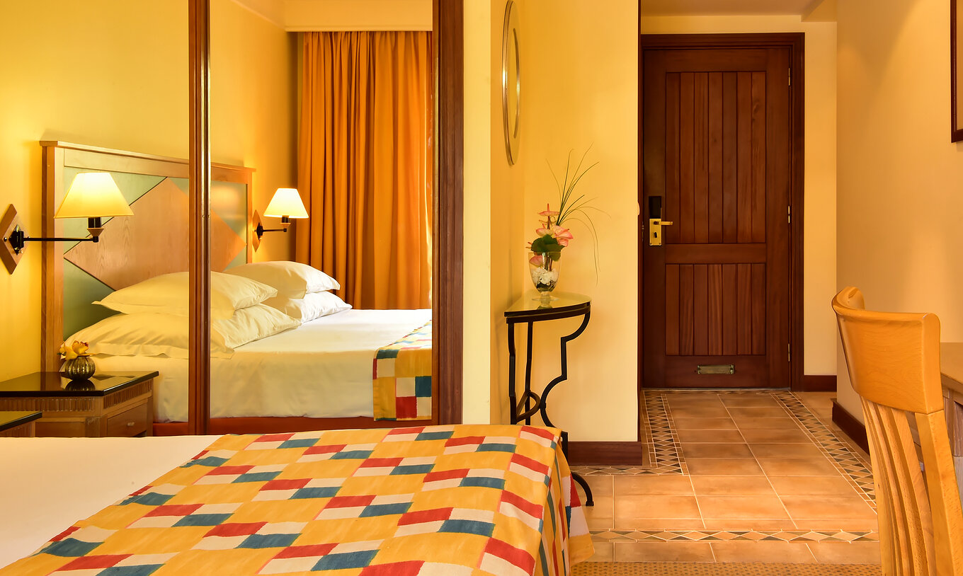 The Superior Room at Pestana Miramar has a double bed with a checkered quilt and a wardrobe with mirror