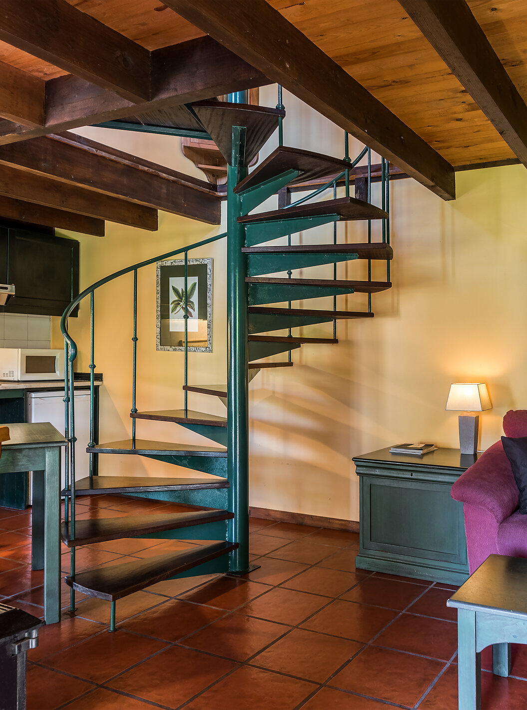 The Duplex Villas of Pestana Quinta do Arco have a sofa with a side table, kitchen, dining table, and metal stairs