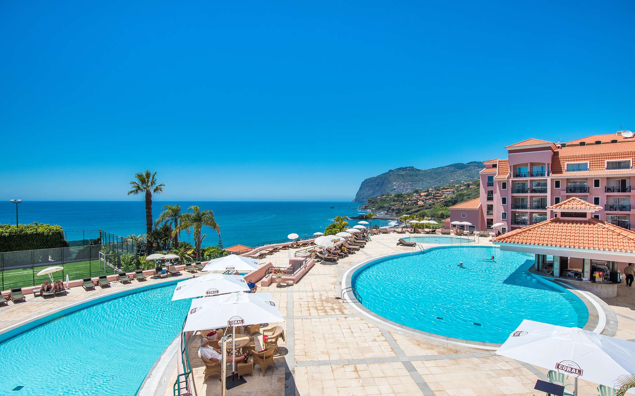 Exterior view of the outdoor pool of Pestana Royal All Inclusive, with the ocean in the background on a clear sky day