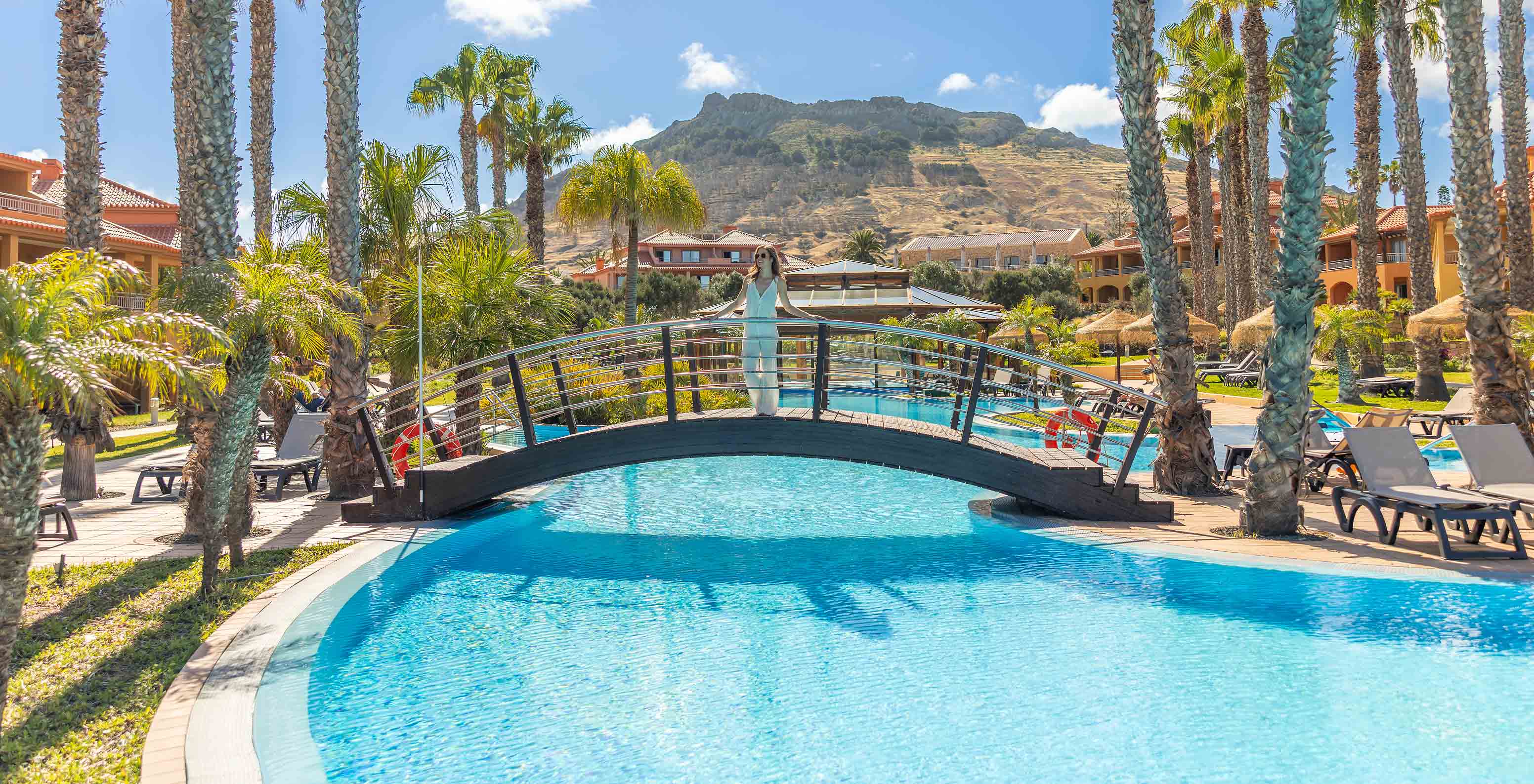 Guest of Pestana Porto Santo hotel standing on the bridge crossing the outdoor pool and surrounded by palm trees