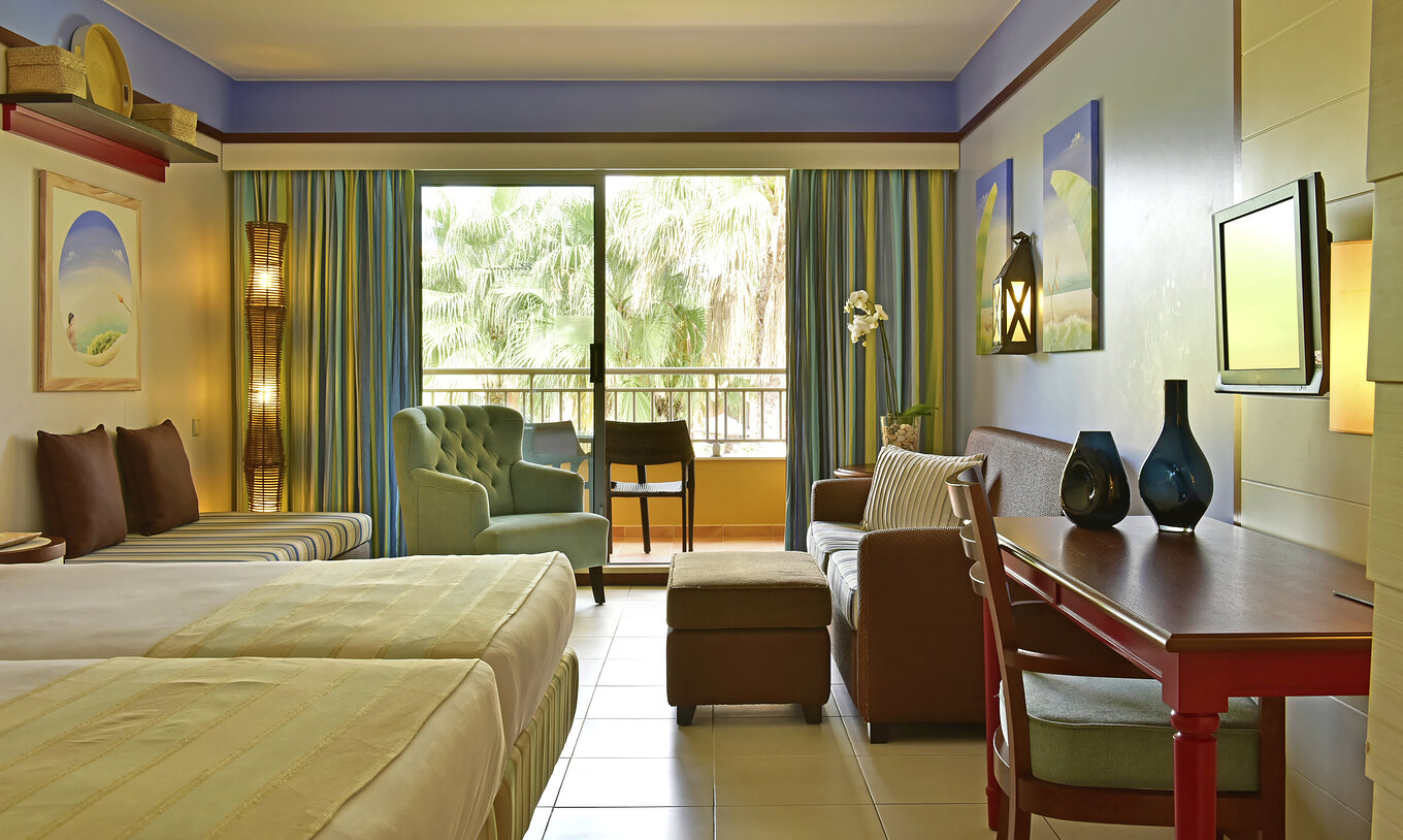 The Family Double of Pestana Porto Santo All Inclusive has two beds, a television, sofas, and a balcony with garden view