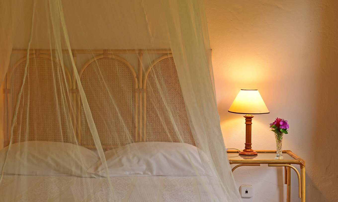 The Classic room at Pestana Miramar São Tomé has a bed with a mosquito net and a bedside table with a lamp on