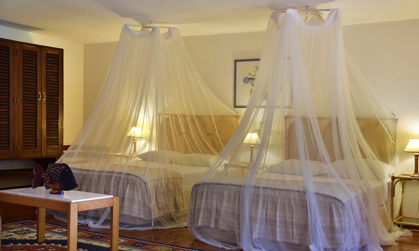 The Junior Suite at Pestana Miramar São Tomé has two double beds with mosquito nets and three bedside tables