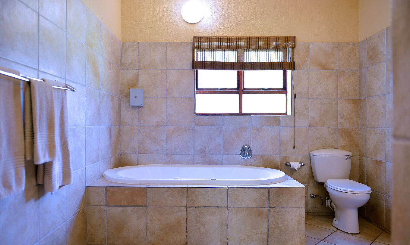 The Rhino Family Cottage at Pestana Kruger Lodge has a beige bathroom with a window, bathtub and toilet