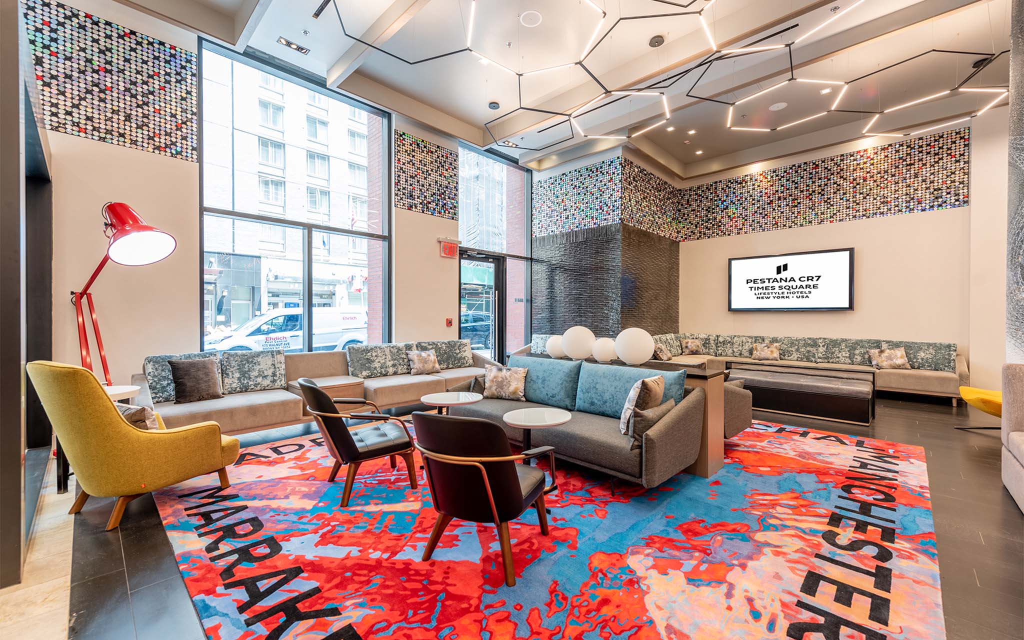 Interior view of the lobby of Pestana CR7 Times Square, with comfortable sofas, chairs, and a vibrant rug