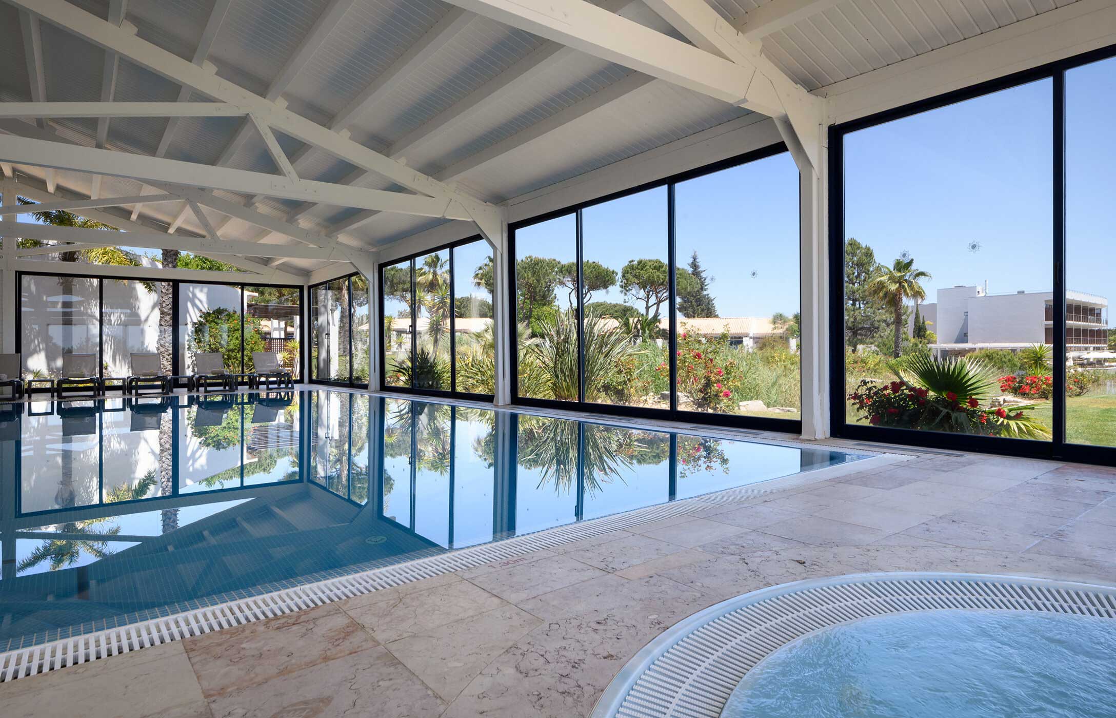 Indoor pool at Pestana Vila Sol Spa with lounge chairs and a view of the garden, highlighting a relaxing atmosphere