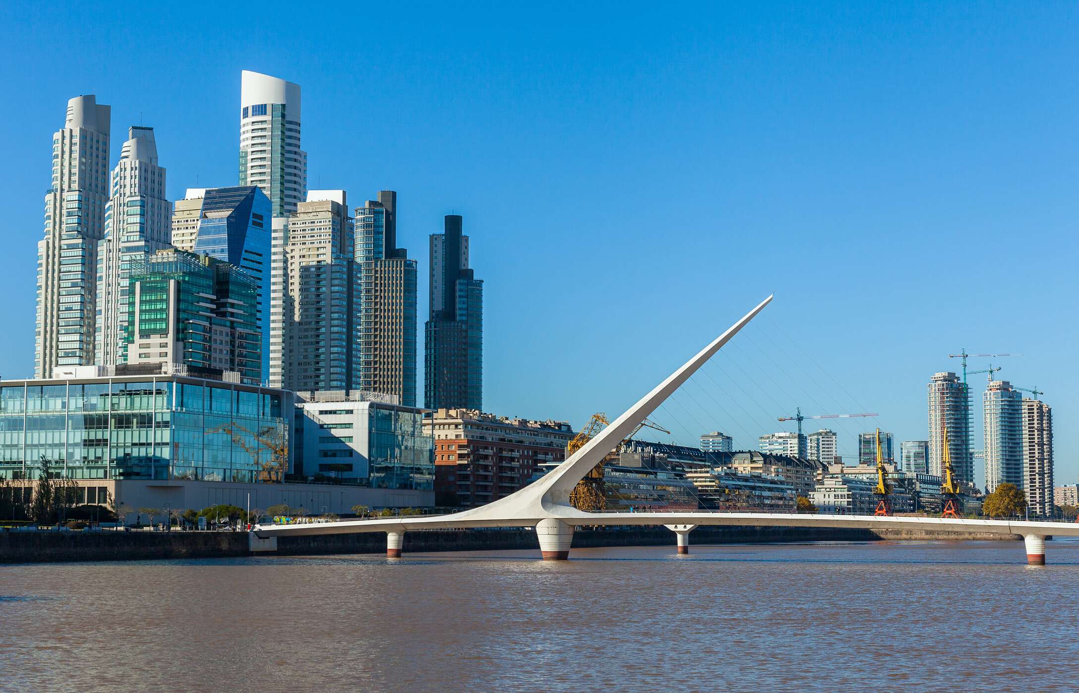 El icónico Puente de la Mujer, en forma de vela, sobre un río en Buenos Aires, con Puerto Madero al fondo