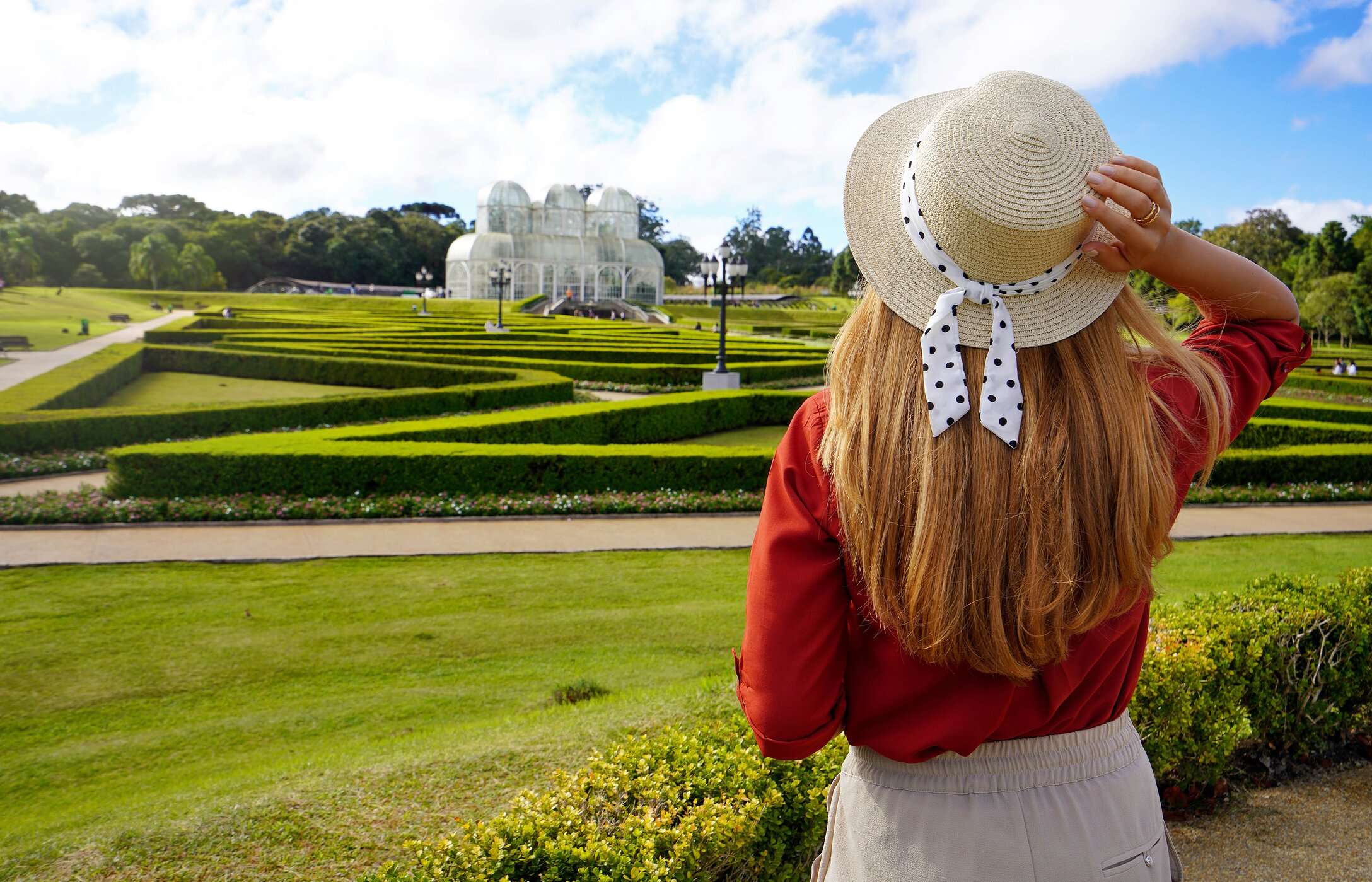 Mujer con sombrero admirando el Jardín Botánico de Curitiba, Brasil, rodeada de césped y vegetación.