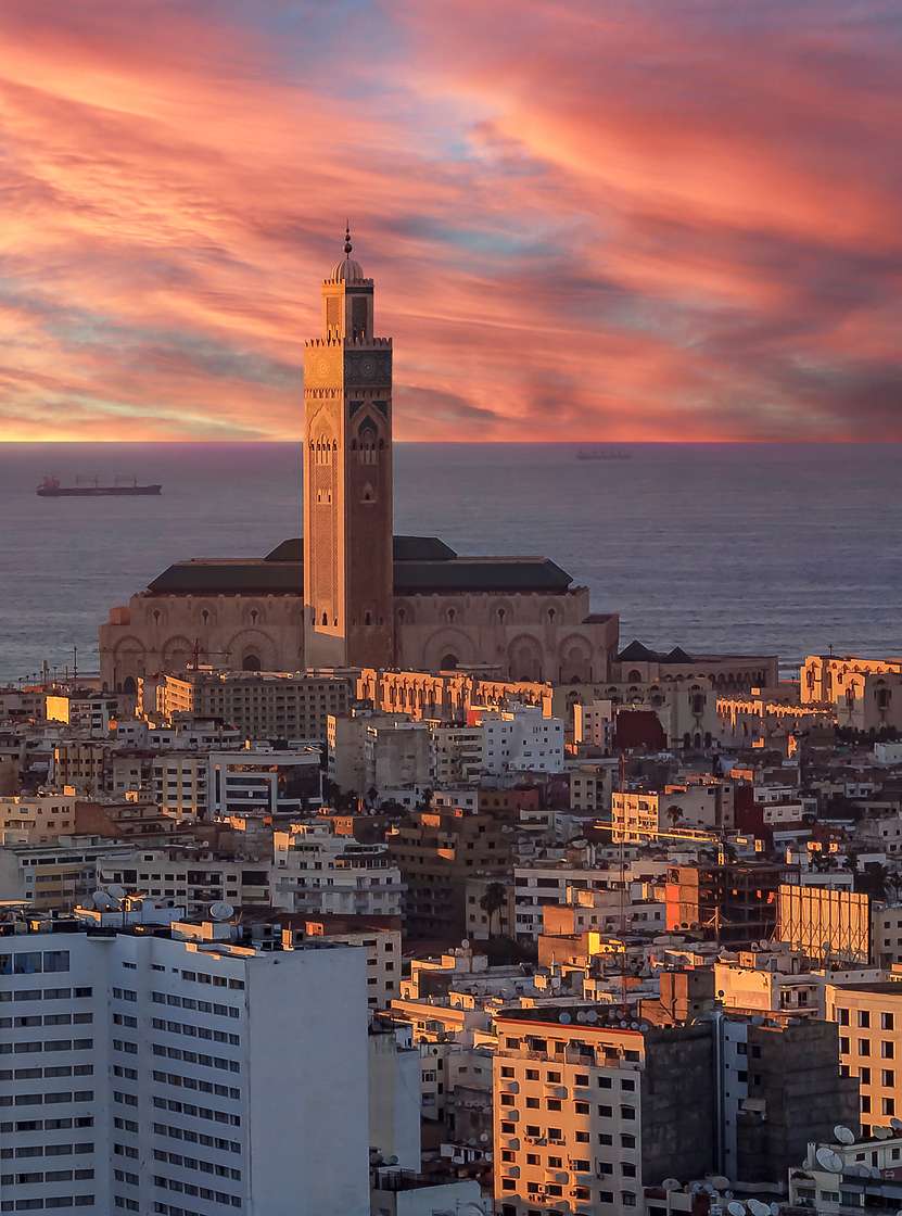 Vista aérea sobre Casablanca, con la luz del atardecer iluminando varios edificios, el cielo sobre el mar y la torre