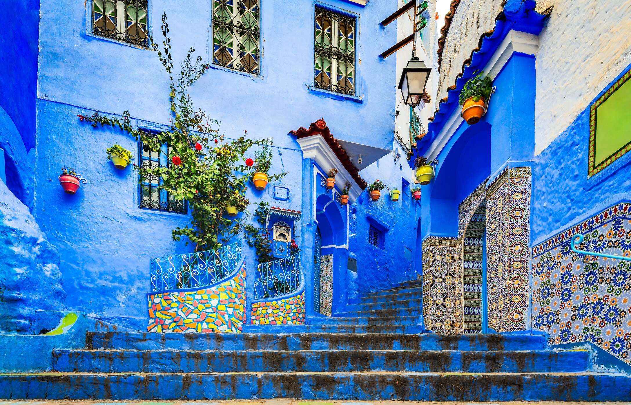 Escalera en Chefchaouen, con edificios azules, azulejos con patrones y macetas colgadas.