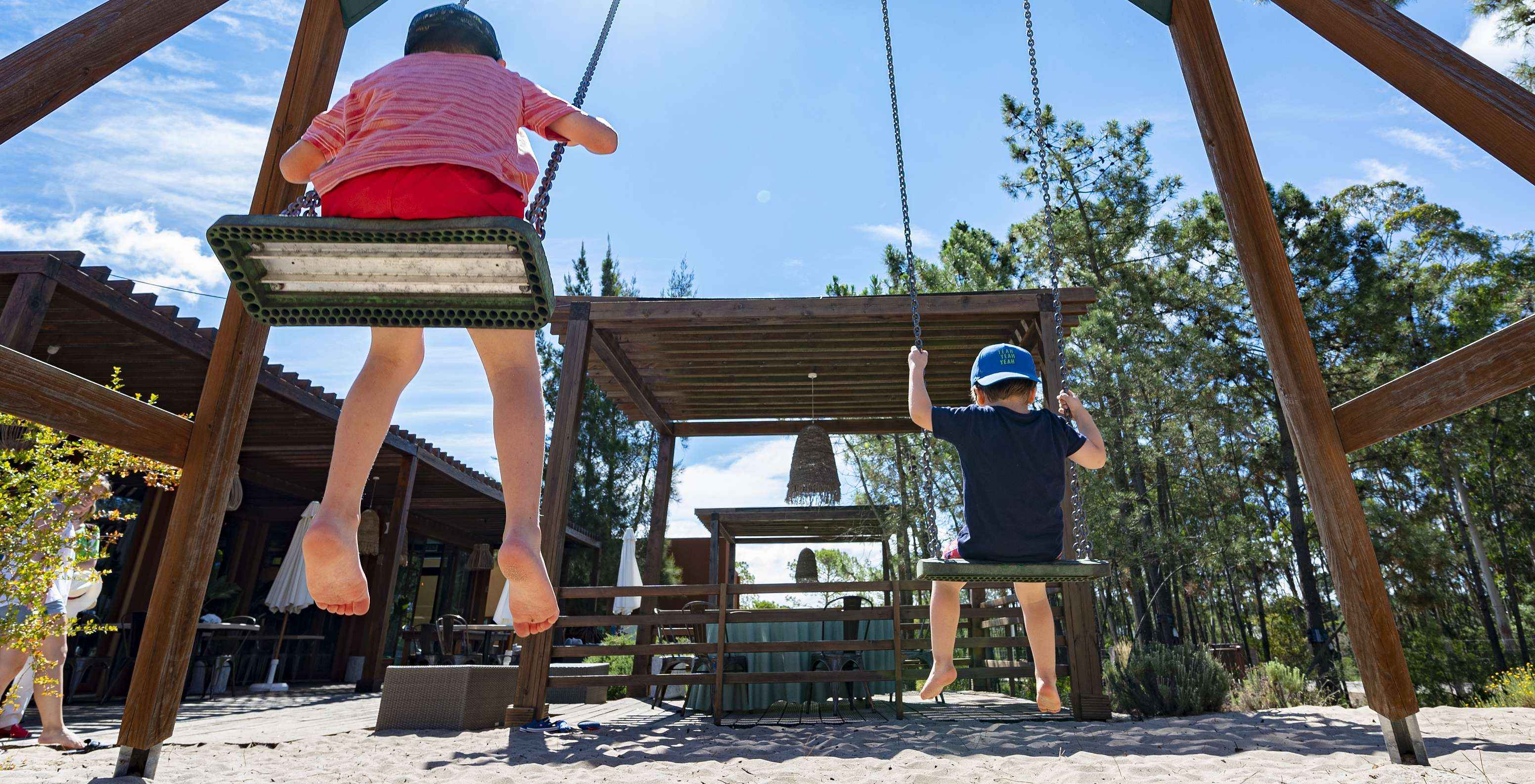 Columpios con dos niños en un pequeño parque infantil, junto al restaurante del Pestana Tróia Eco Resort